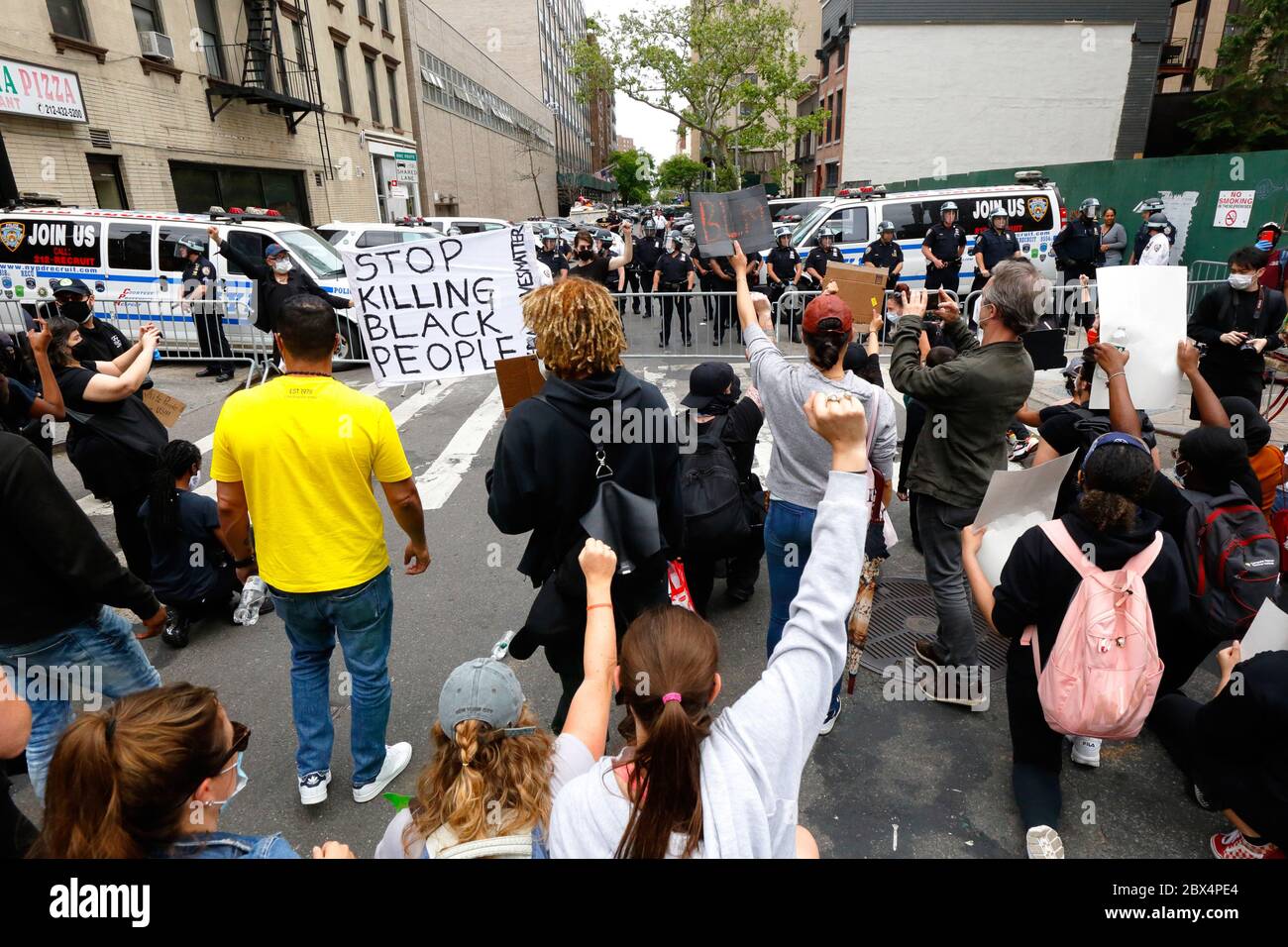 New York, NY 2 juin 2020. Les gens s'arrêtent brièvement dans une rue résidentielle barricadée pour se mettre à genoux et élever des poings dans les airs à la police en poste ; deux personnes sont également munies d'un panneau « Top Killing Black People ». Les gens marchent en solidarité avec d'autres dans tout le pays en appelant à la justice dans une série récente de meurtres de la police américaine : George Floyd, Breonna Taylor et d'innombrables autres. Des milliers de personnes se sont jointes à la marche depuis Foley Square, s'arrêtant près de Gracie Mansion, la maison du maire de New York, avant de déménager à Times Square plus tard dans la soirée. 2 juin 2020 Banque D'Images