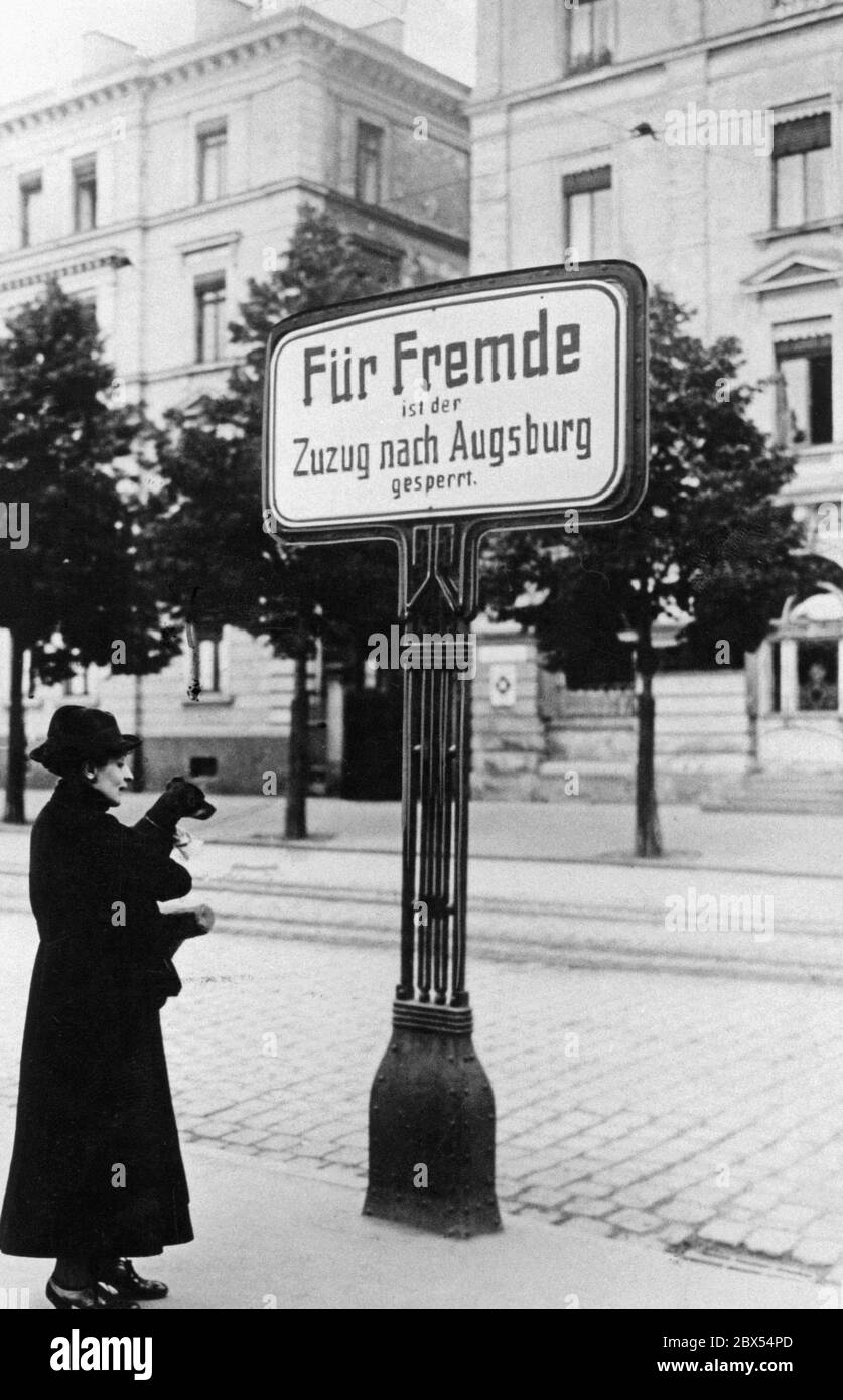 Une femme, avec un chien dans ses bras, se tient dans une rue en face de la gare d'Augsbourg, devant un panneau indiquant que « le déménagement à Augsbourg est fermé pour les étrangers ». En raison du manque de logements, de nombreuses grandes villes ont résisté à l'immigration de l'extérieur de la ville après la première Guerre mondiale. Le panneau d'avertissement est destiné à dissuader les nouveaux arrivants. Banque D'Images