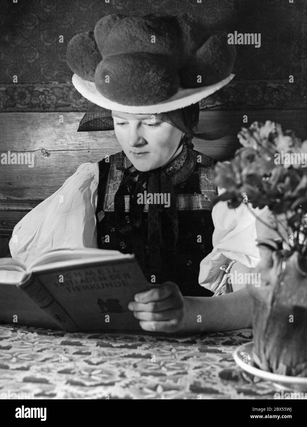 Une jeune femme de la vallée de Gutach dans la Forêt Noire portant un costume traditionnel folklorique et Bollenhut est assise à une table et lit le « Leitfaden der Tierkunde » d'Otto Schmeil. La photo a probablement été prise dans les années 1930. Banque D'Images