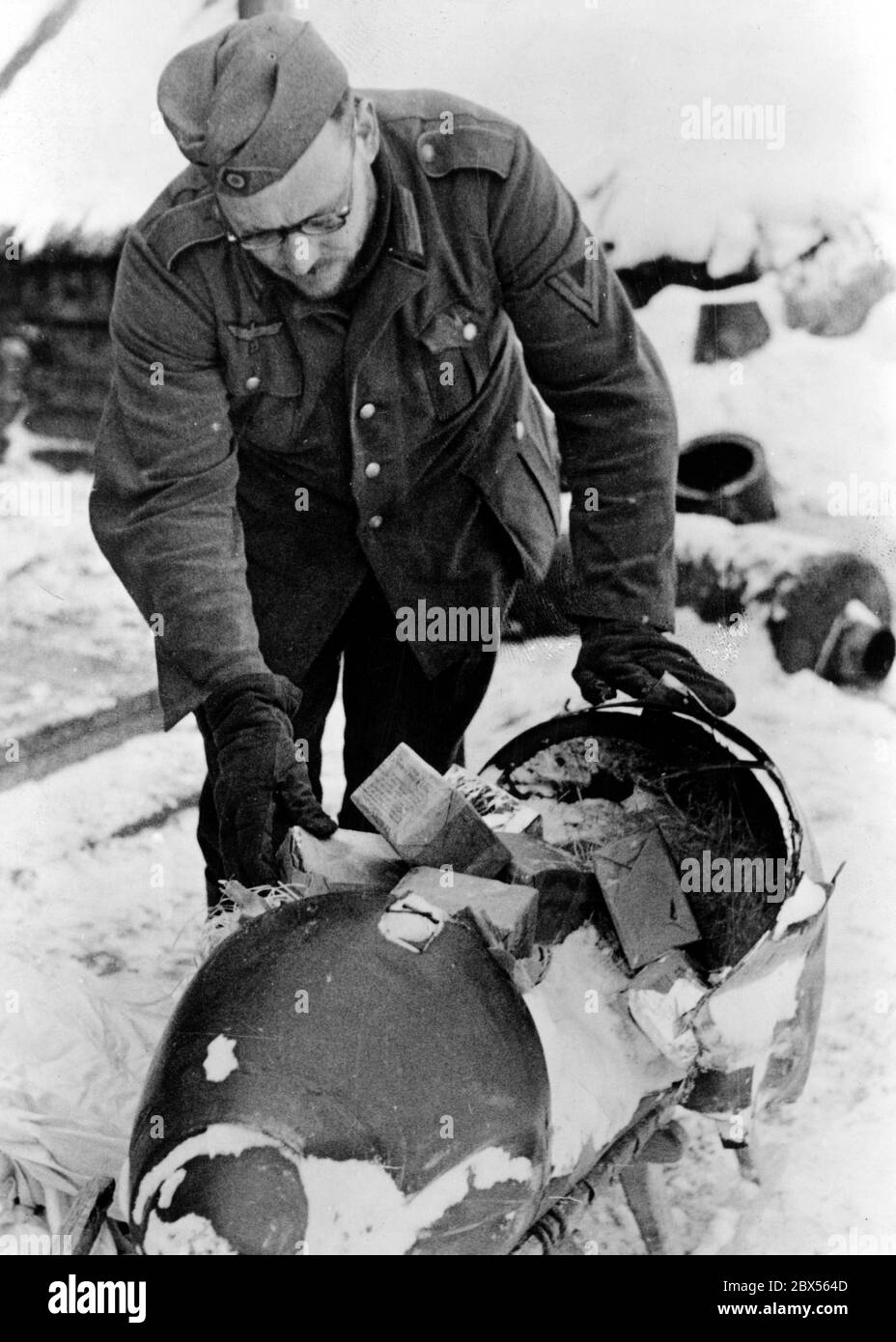 Un soldat allemand examine la bombe de provisions qui a craqué sur l'impact. En larguées quotidiennement de telles « bombes », les soldats allemands encerclés de Kholm ont été approvisionnés en nourriture, munitions et équipements depuis les airs pendant plus de 3 mois. Pendant la bataille d'encerclement de Kholm, le 'Kampfgruppe Scherer' a défendu avec succès la ville pendant 105 jours. (Photo de la compagnie de propagande (PK) par le correspondant de guerre Richard Muck, qui a pris l'avion dans la poche au début du mois de mars). Banque D'Images