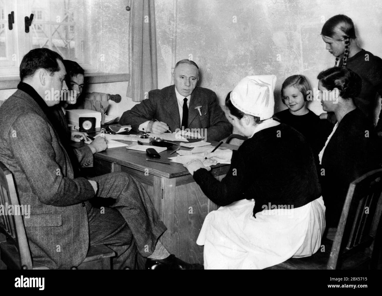 Le professeur Peter Muehlens (au centre) de l'Institut tropical de Hambourg donne des conseils médicaux aux 462 Allemands qui ont été expulsés de l'ancienne Afrique de l'est allemande par l'Angleterre. La photo montre une famille avec des enfants dans la clinique de Muehlens, où une infirmière est également présente. Banque D'Images