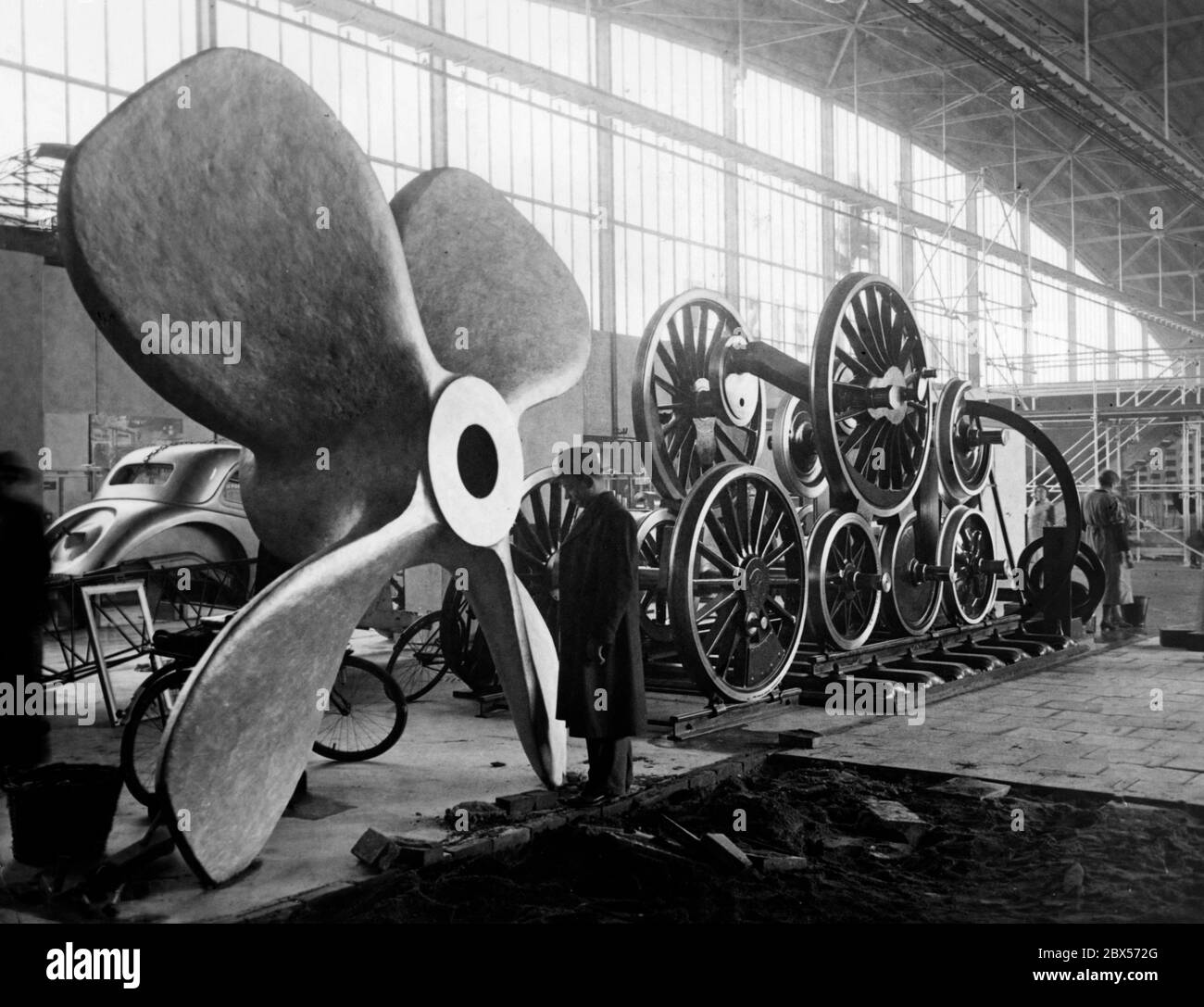 A l'ouverture de l'exposition Reich 'Shaffendes Volk' ('Creative People') à Düsseldorf, un visiteur regarde l'hélice d'un navire. Sur la droite se trouvent les énormes roues d'une locomotive. Sur la gauche, en arrière-plan, se trouve le toit d'une voiture de tourisme. Banque D'Images