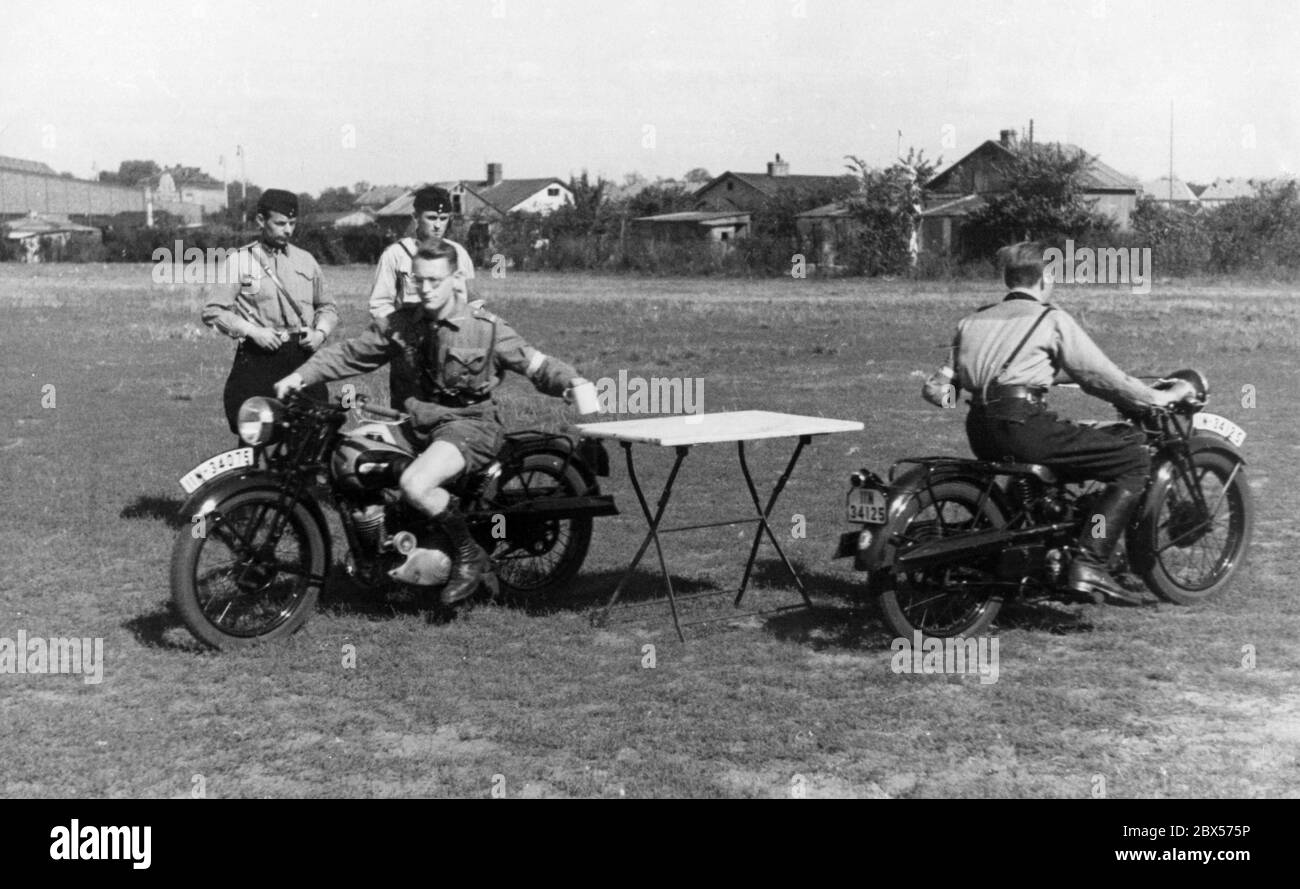Membres du HJ moteur lors d'un test d'aptitude sur moto avec des tasses à café dans leurs mains. Deux membres du NSKK regardent le test. Les motos sur lesquelles les cavaliers sont assis sont de type DKW SB 200 Gelaendesport. Banque D'Images