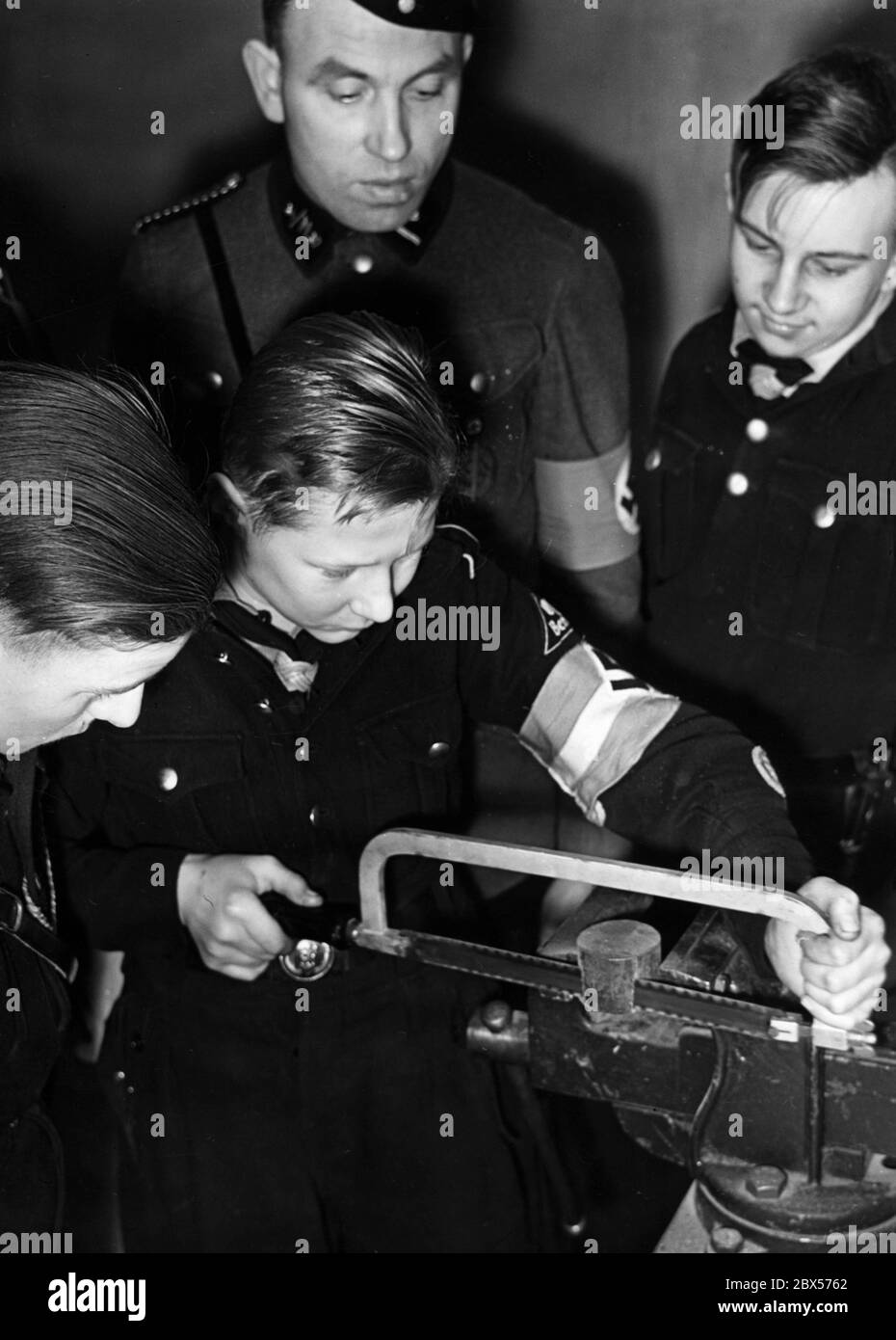 Au cours d'une leçon d'atelier de la Jeunesse de Motor Hitler un garçon scie un morceau de métal. Derrière lui, il y a un NSKK qui regarde par-dessus son épaule. Deux autres membres de la jeunesse hitlérienne regardent aussi. Banque D'Images