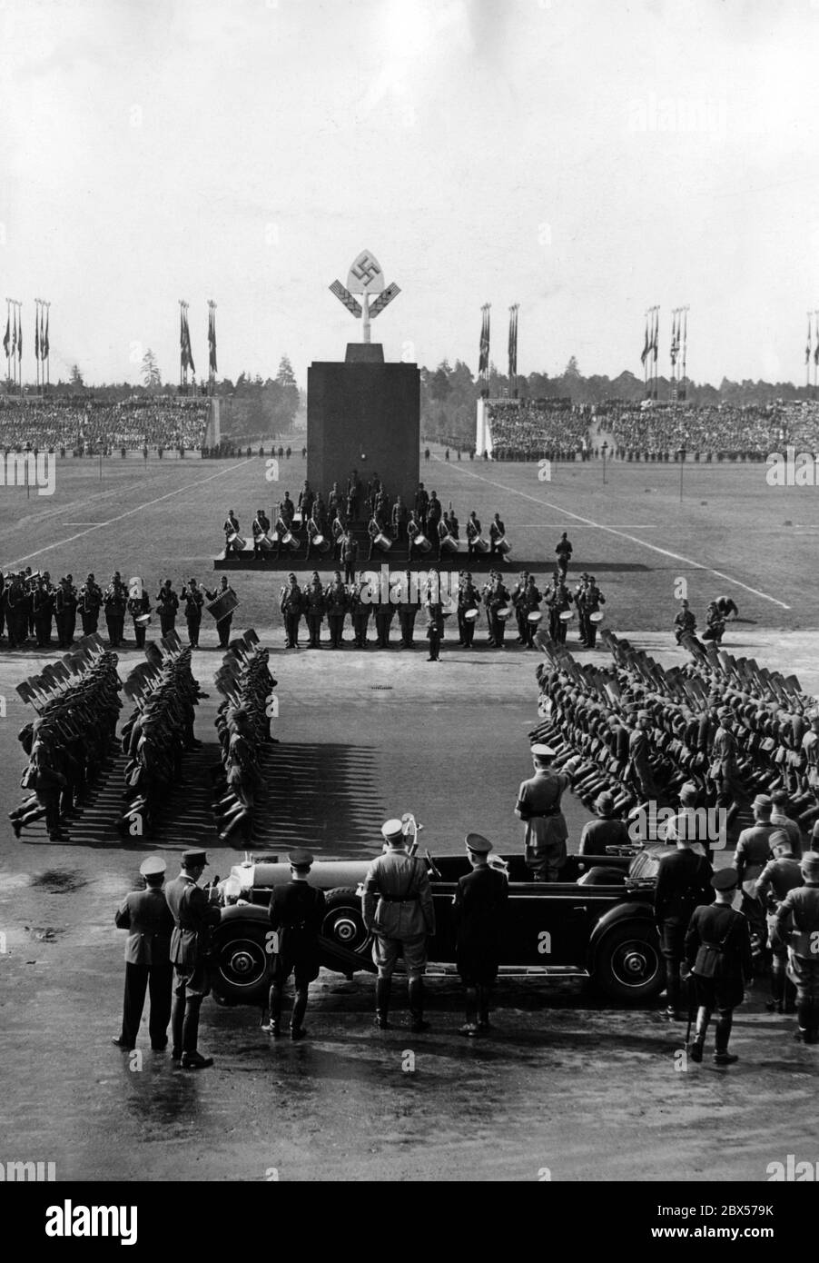 Adolf Hitler, debout dans une Mercedes sur le Zeppelinwiese, prend le salut des formations du Reich Labour Service marchant avec leurs pique. En arrière-plan, des groupes de batteurs et le mémorial du travail. Banque D'Images