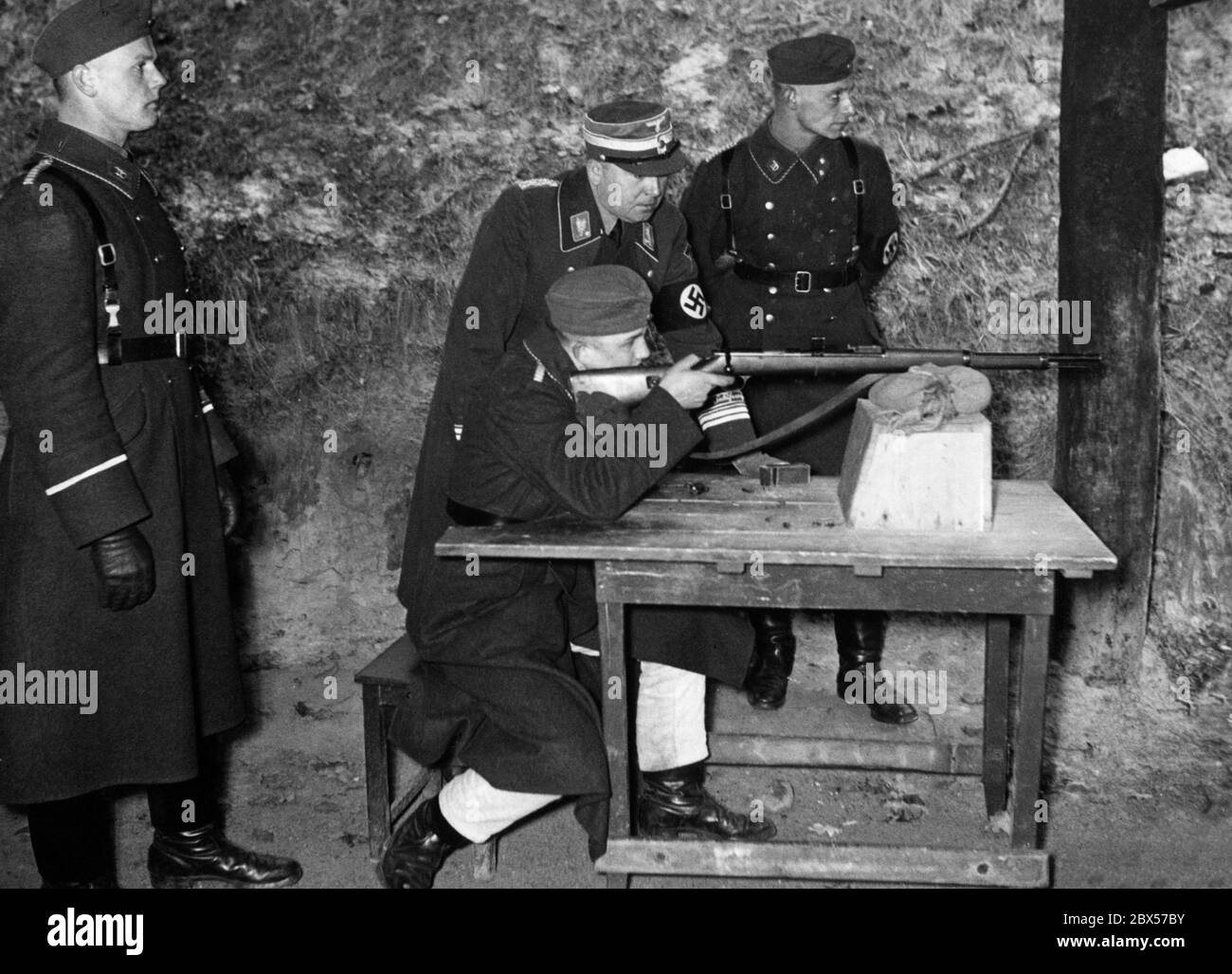 Membre sa de Sturmbann 1 de la Wachstandarte Feldherrnhalle tirating avec un fusil 98K au champ de tir. Reimann, chef de brigade, est en visite et observe la pratique du tournage. Banque D'Images