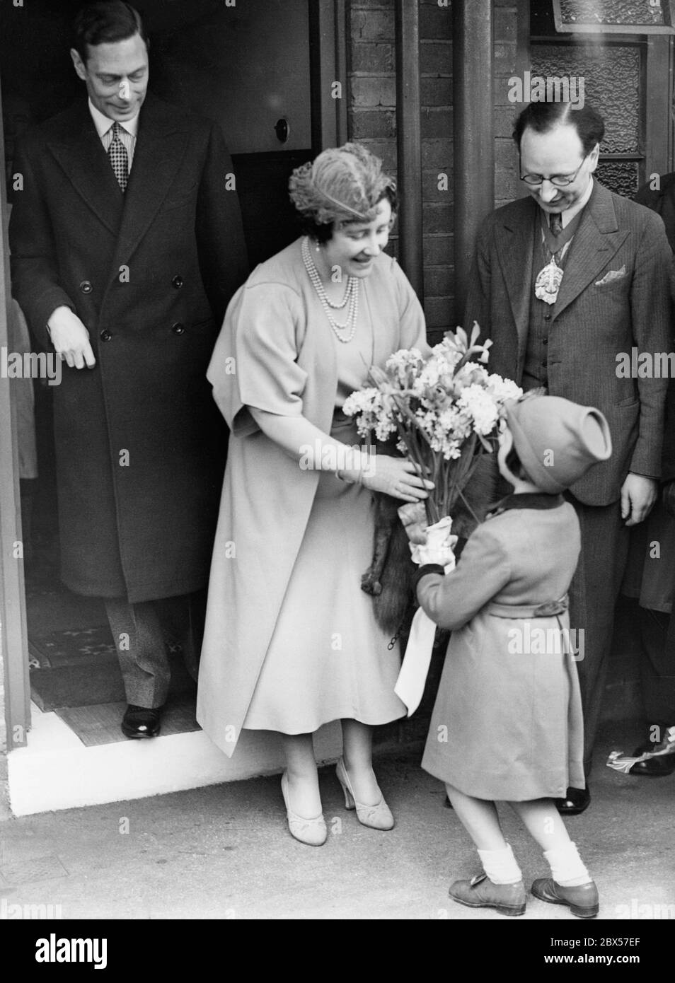 La reine Elizabeth reçoit un bouquet de fleurs d'une petite fille nommée  Frances Neil, tandis qu'elle et son mari, le roi George VI, visitent Hilcot  House, dans la rue Clarissa, depuis Kingsland