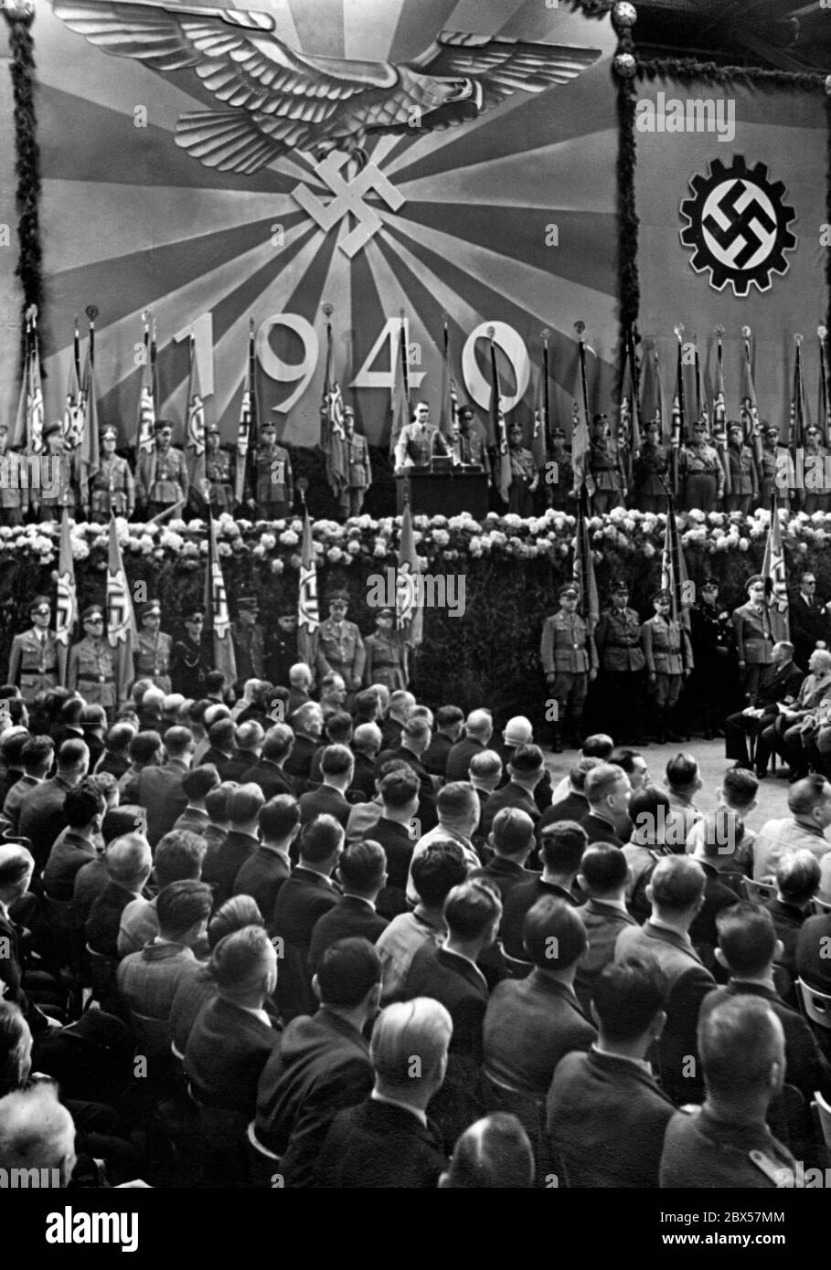 Rudolf Hess prononce un discours à Essen dans un atelier de locomotive de la société Krupp. La croix gammée dans la roue dentée est l'emblème du Front travailliste allemand, le drapeau de l'usine. Banque D'Images