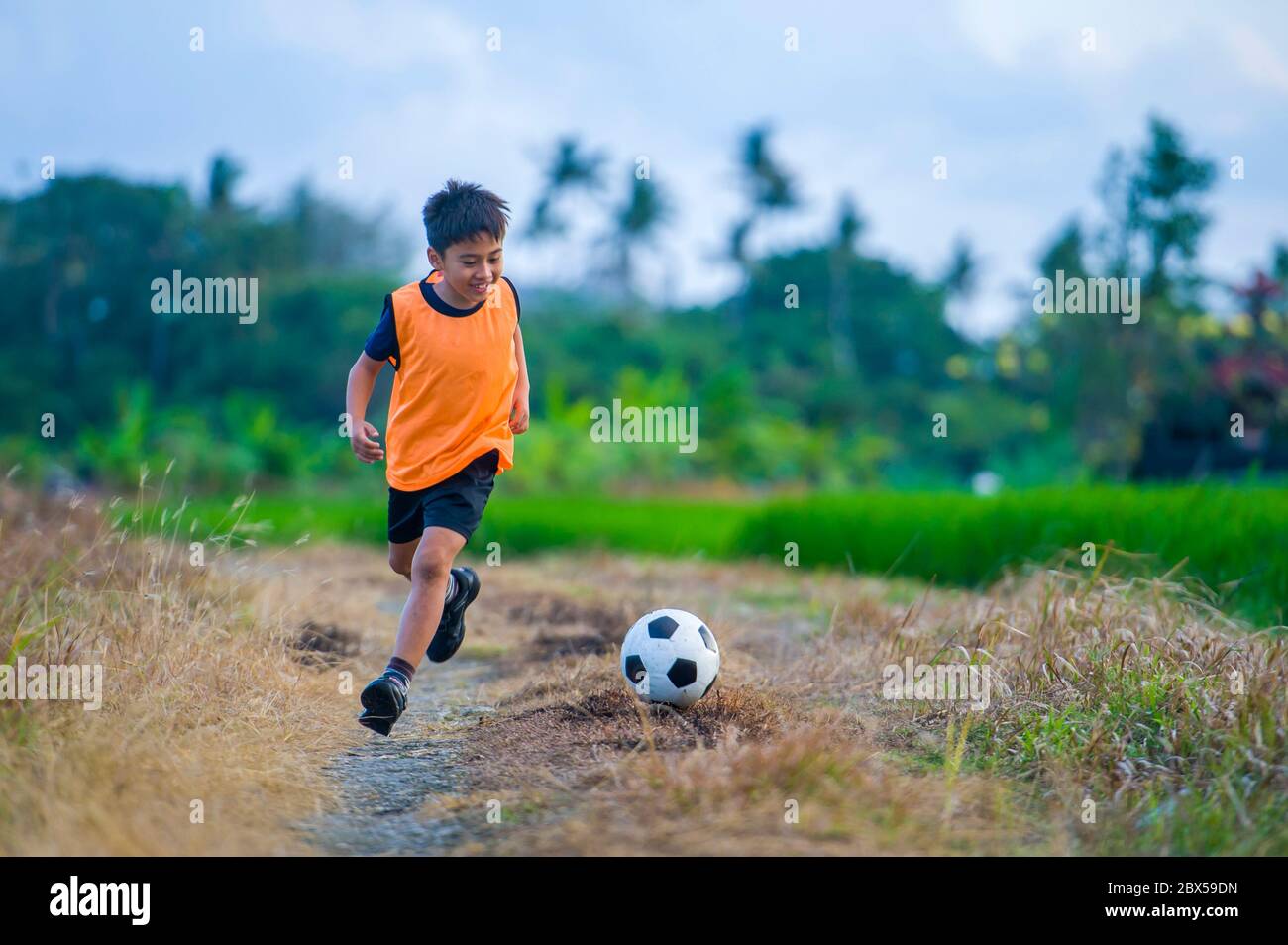 8 ou 9 ans heureux et excités enfant jouant au football en plein air dans le jardin portant la veste d'entraînement de course à pied et de kicking football ball, l'enfant ayant le plaisir Banque D'Images