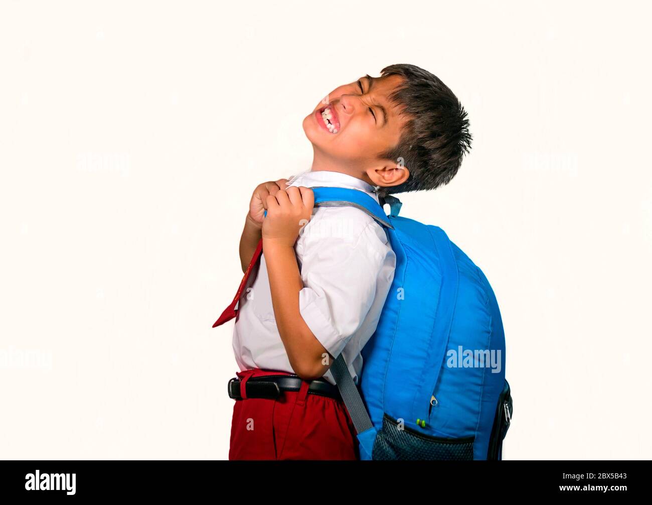enfant doux de 7 ou 8 ans dans un sac de transport uniforme plein de livres se sentant contrarié et se plaignant du poids du sac à dos dans l'école paresseuse unha Banque D'Images