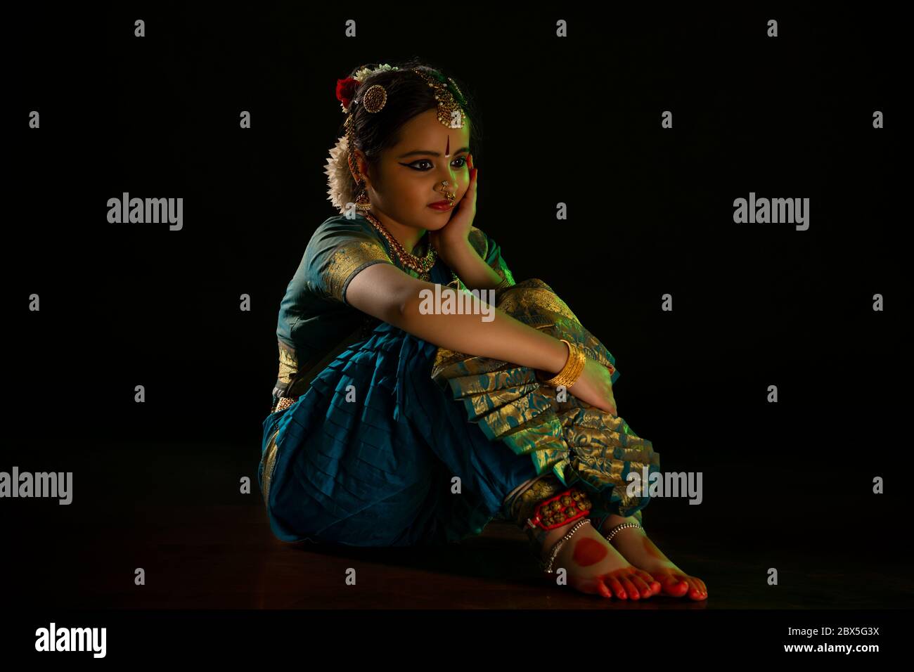 Jeune danseuse de bharatnatyam assise pendant sa représentation devant un fond noir. Banque D'Images