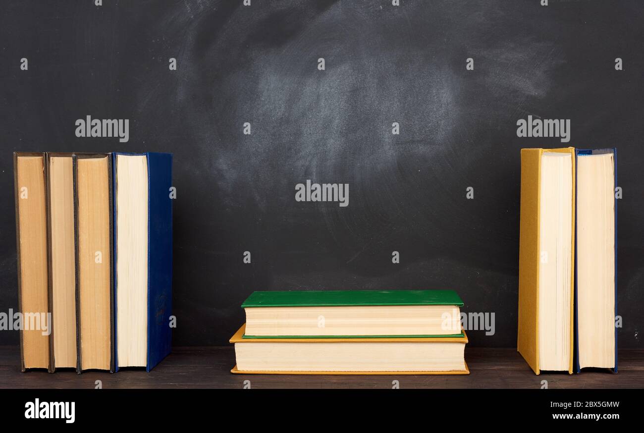 pile de divers livres de hardback sur le fond d'un tableau noir vide de craie, place pour le texte, de retour à l'école Banque D'Images