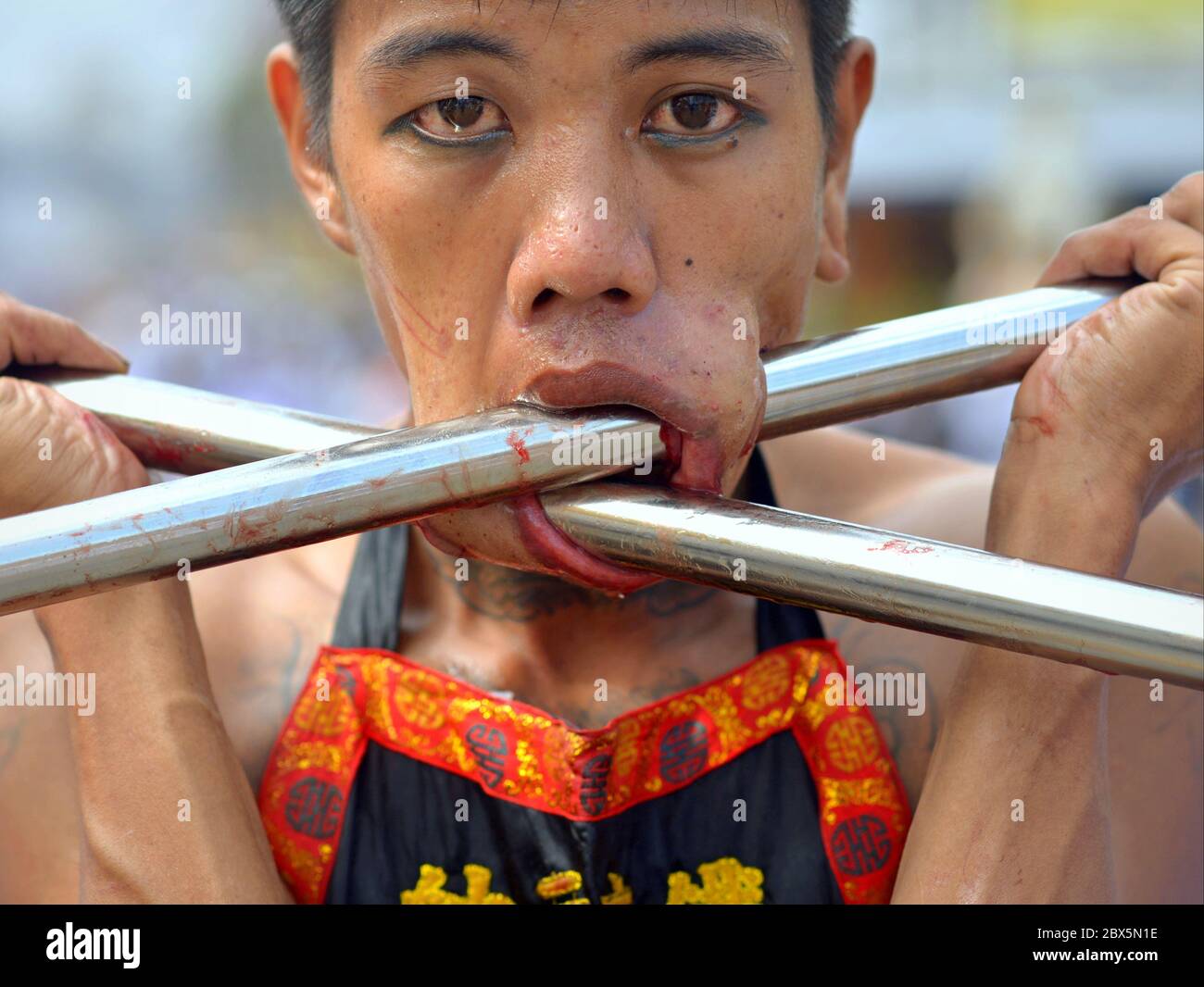 Le dévot taoïste chinois thaïlandais pière ses joues avec deux longues pipes en acier inoxydable pendant le Festival végétarien de Phuket (Festival des neuf dieux des Empereurs). Banque D'Images