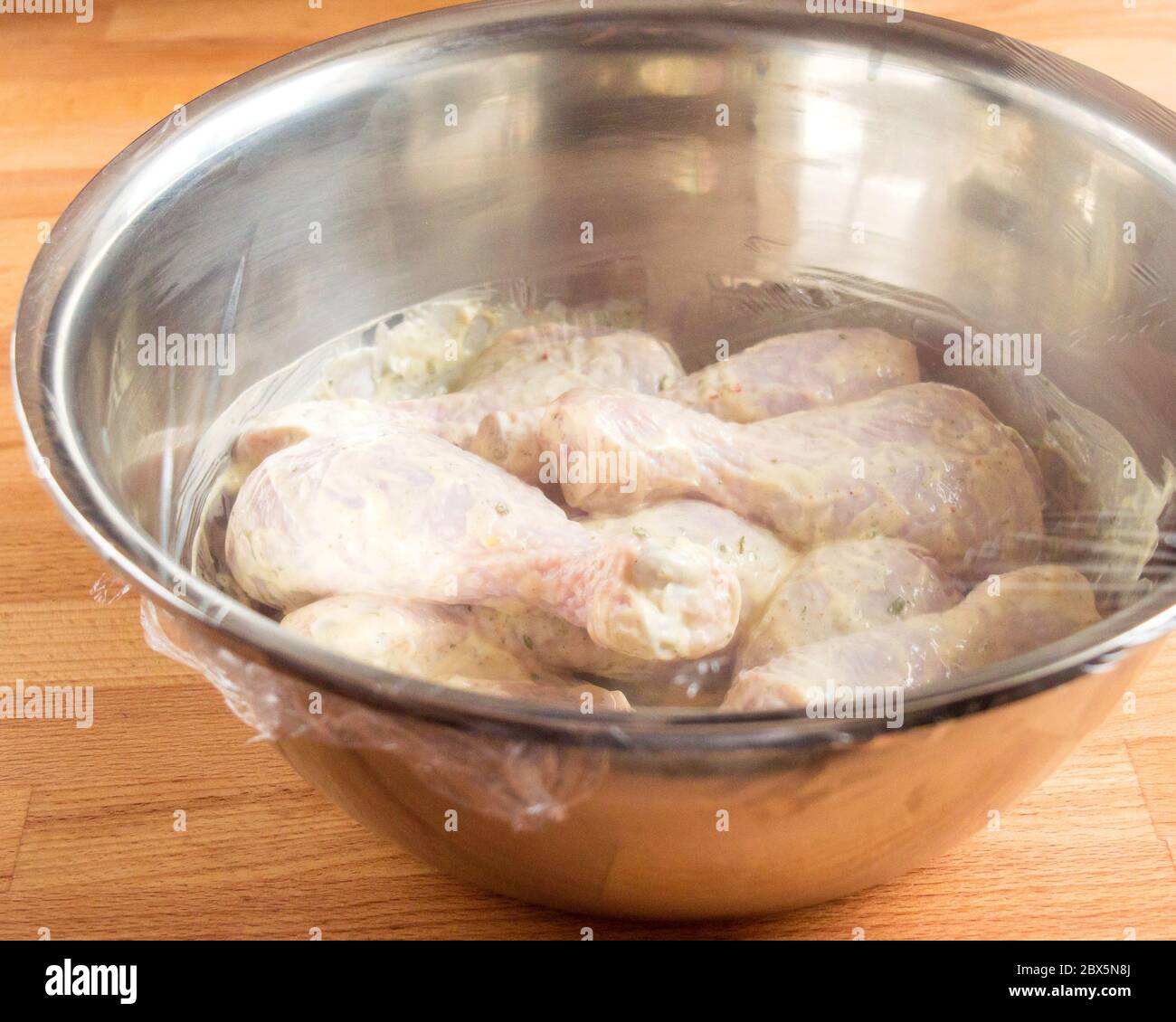 Pilon de poulet imbibé de mayonnaise. Un bol de poulet dans la sauce est recouvert d'un sac de cuisine transparent. Banque D'Images