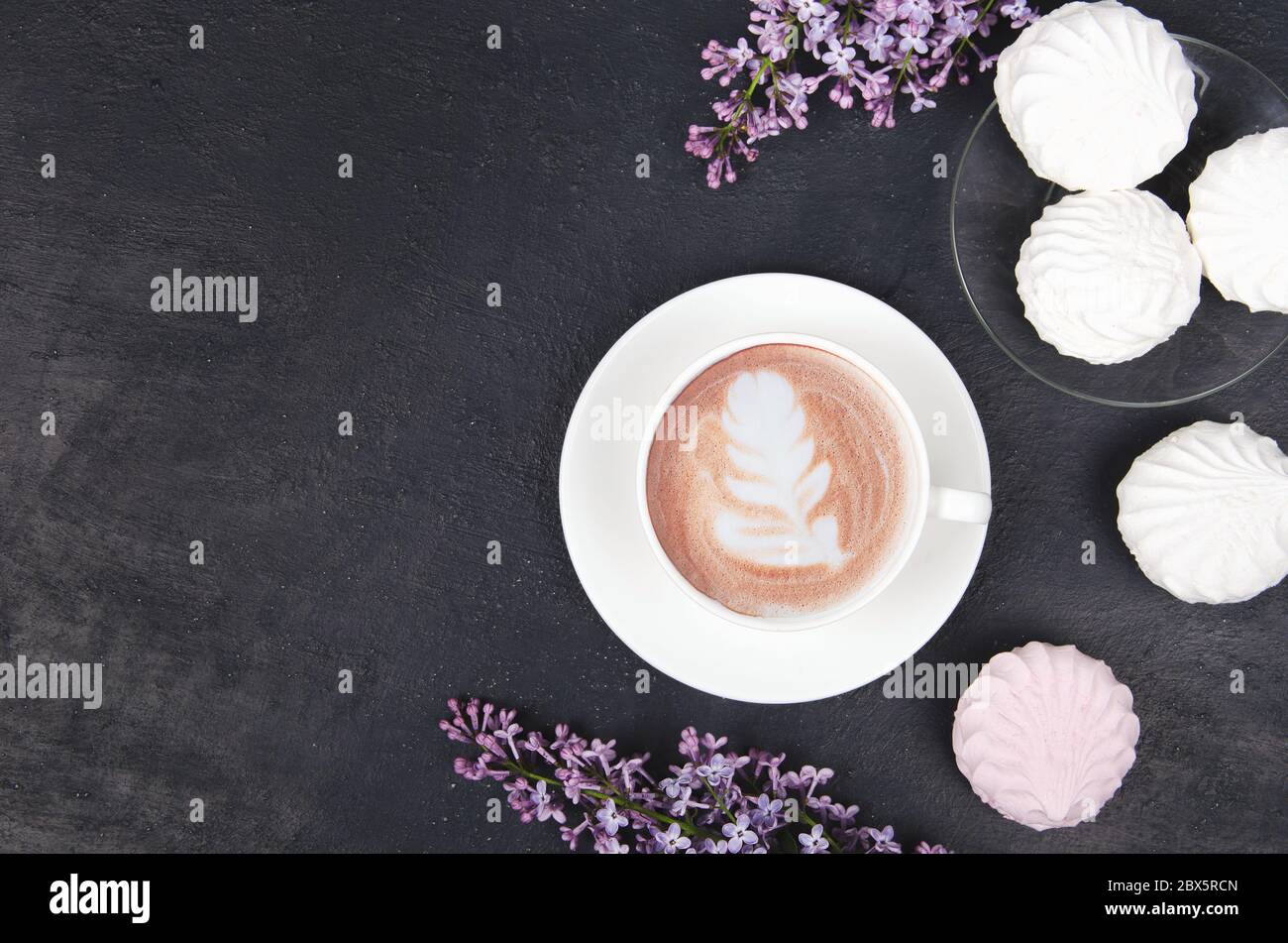 Lilas, café avec latte art et guimauves sur table noire. Repose-plan romantique avec espace pour copier Banque D'Images