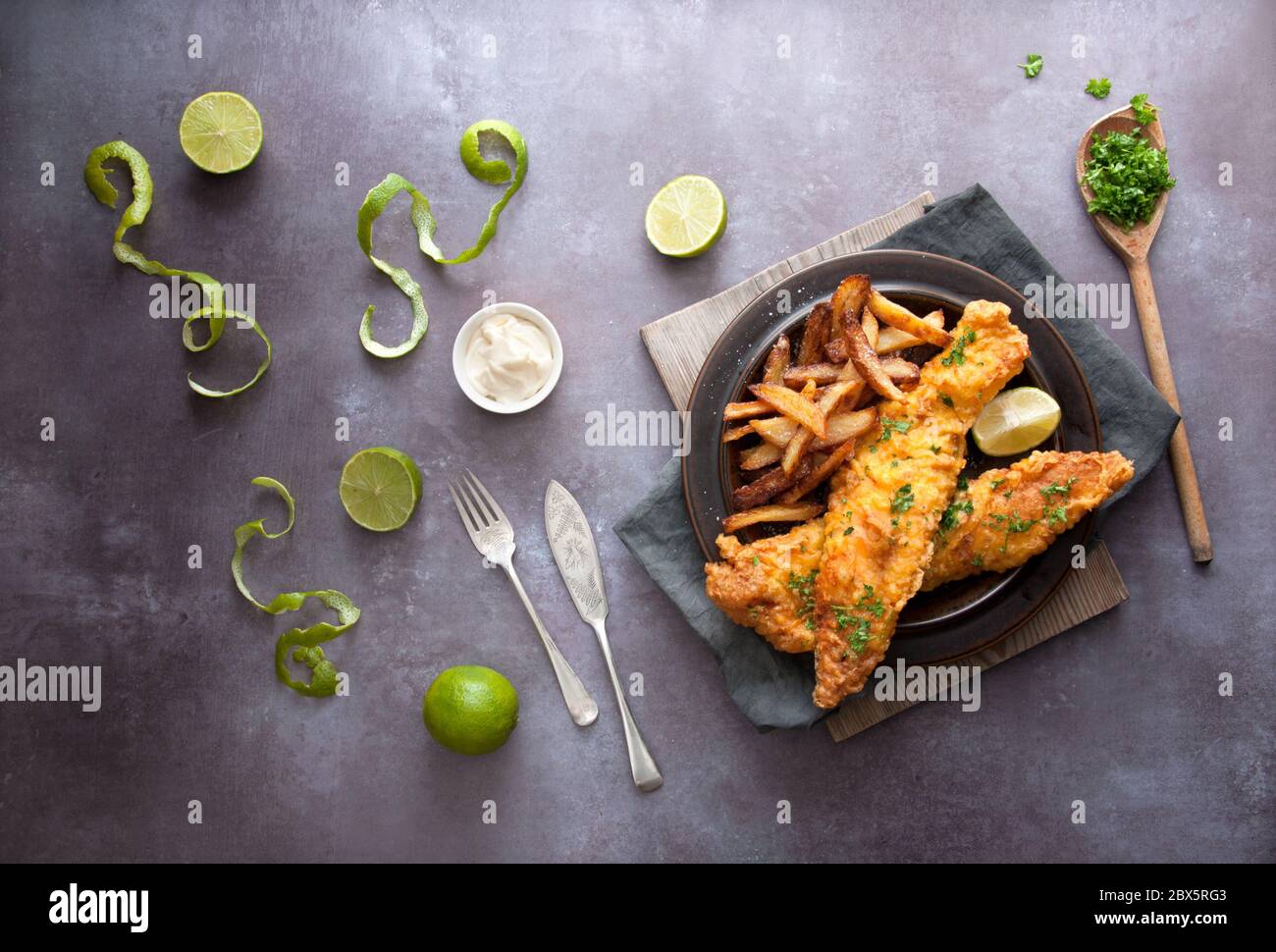 Poisson frit en pâte avec des frites coupées à la main, du persil et du citron vert Banque D'Images
