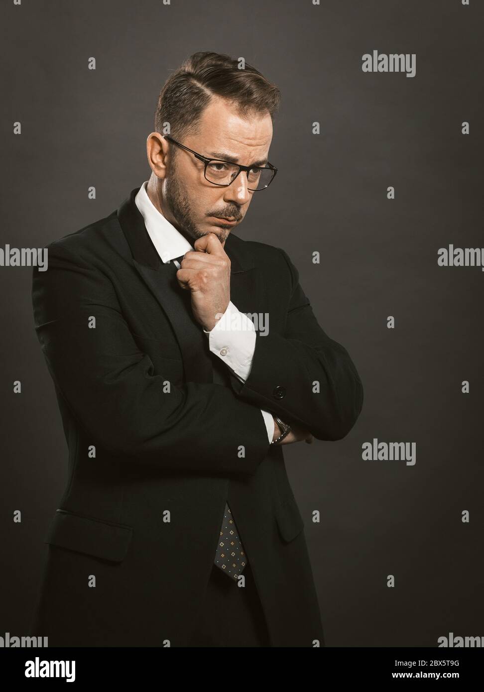 Un homme d'affaires doué a traversé les bras en touchant son menton. Homme intelligent et réfléchi en lunettes se tient à regarder de côté. Concept de doute Banque D'Images