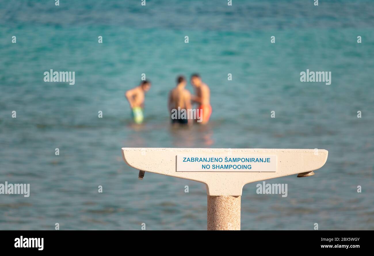 Douche publique sur la plage bacvice avec un panneau d'avertissement qui interdit l'utilisation de shampooing en public.personnes sur la plage dans la distance Banque D'Images
