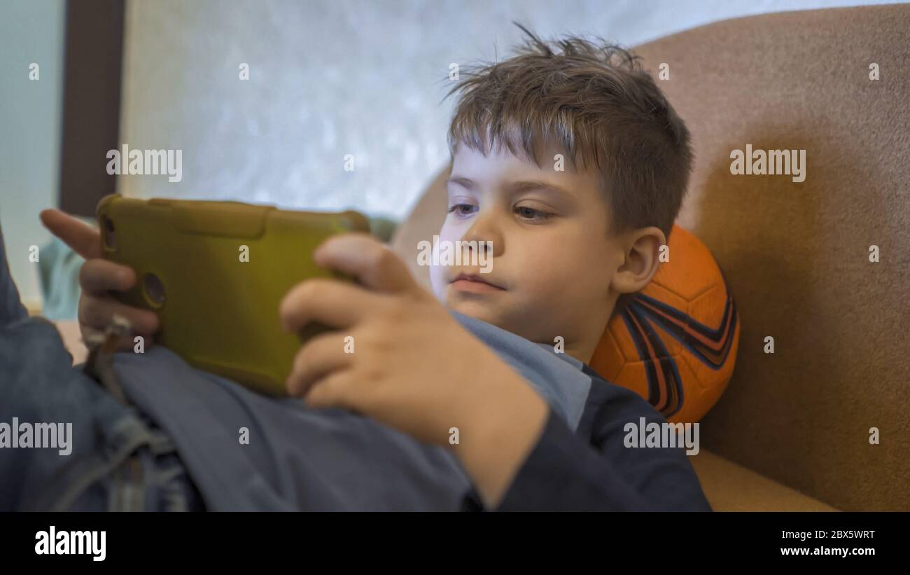 Préchoix utilisant un téléphone portable à la maison. Un garçon caucasien regarde des photos dans un smartphone tout en étant allongé sur un canapé Banque D'Images
