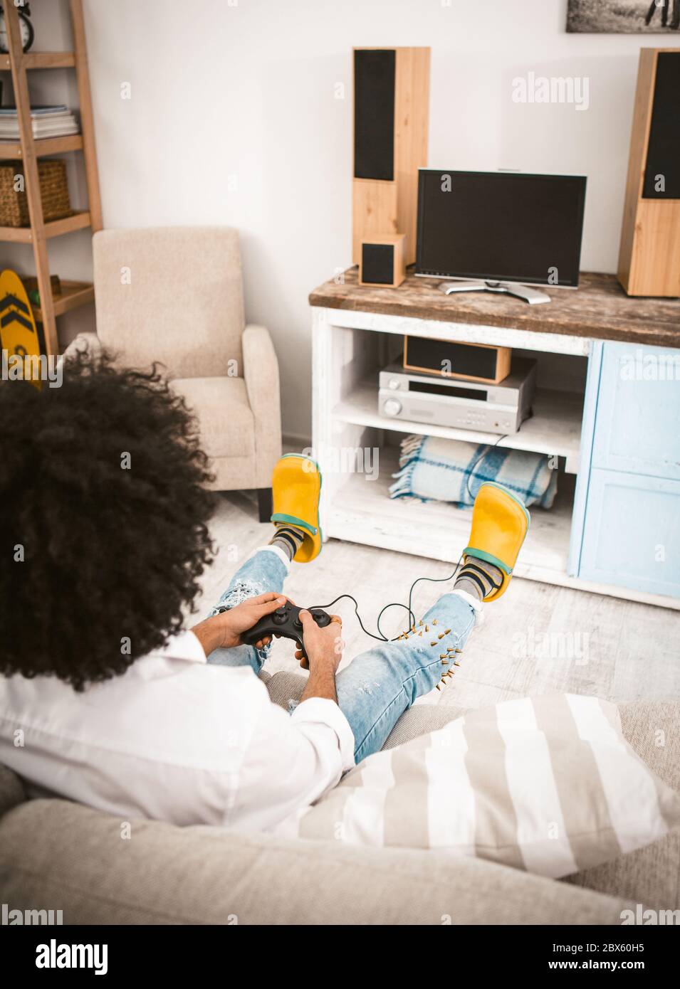 Jeune homme jouant à des jeux d'ordinateur assis à la maison sur un canapé devant la télévision. Vue arrière des boutons de retrait de la manette de la station de jeu non reconnaissables Banque D'Images