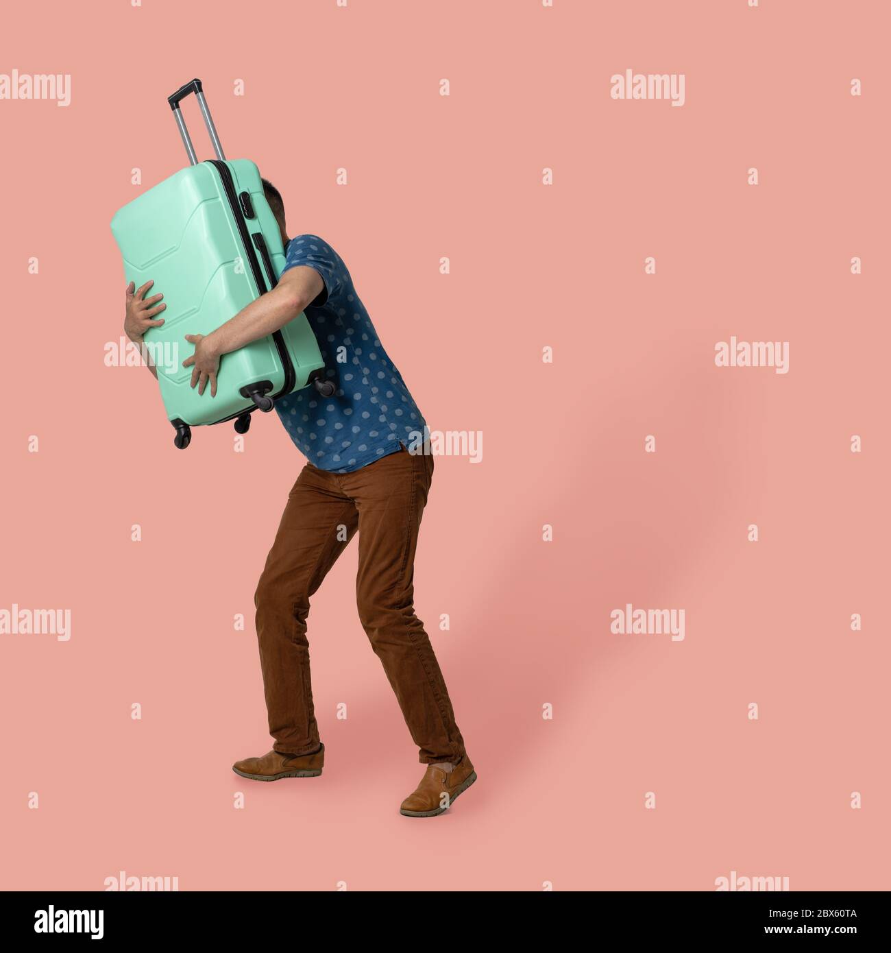 L'homme encadre une valise qui la tient devant lui tout en posant sur un fond coloré. Un homme de race blanche dans un t-shirt et un pantalon marron va en voyage Banque D'Images