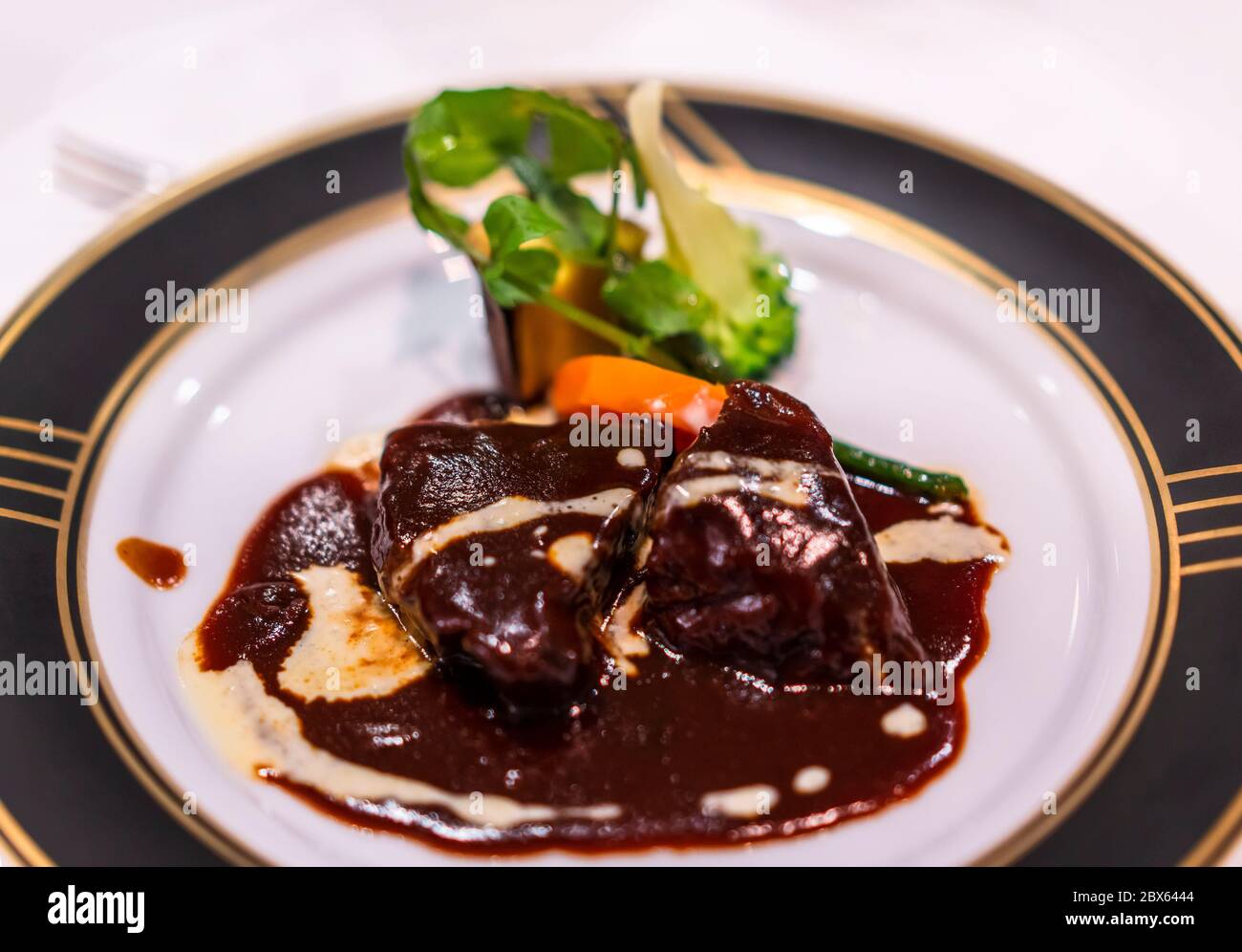 Plat principal français avec ragoût de viande de bœuf bourguignon mijoté dans une sauce au vin rouge avec des légumes comme des carottes sur une assiette à dîner blanche et noire avec ged Banque D'Images