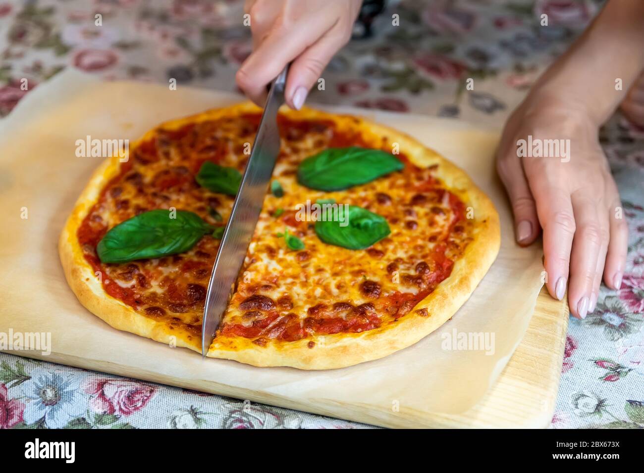 Une femme en gros plan coupe à la main cuite savoureuse pizza italienne maison chaude à Margarita sur un panneau en bois et une table avec un couteau ordinaire. Mozzarella fondue Banque D'Images