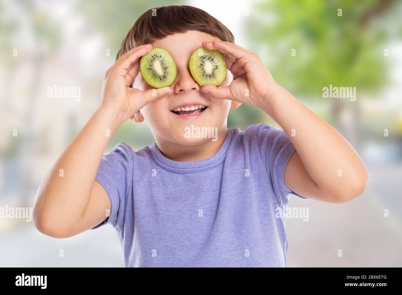 Petit garçon enfant avec kiwi fruit ayant plaisir ville heureux bonheur saine manger à l'extérieur Banque D'Images