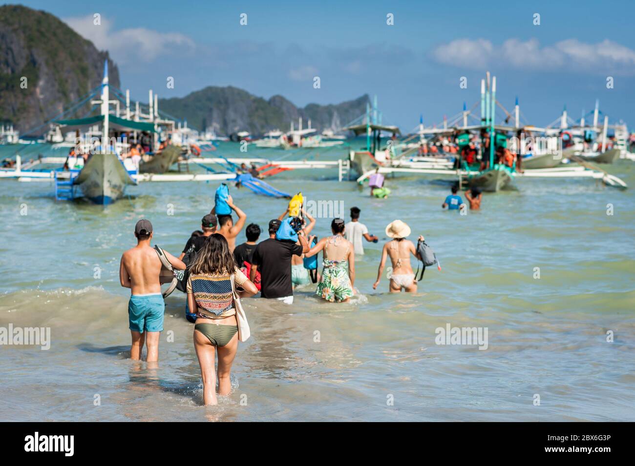 Les touristes à la plage de la ville d'El Nido se sont enlarés vers les nombreux bateaux à longue queue amarrés dans le surf attendant de visiter les îles et les plages. Banque D'Images