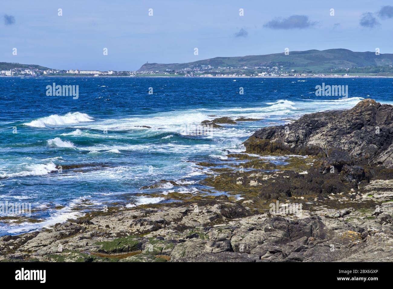 En regardant de l'autre côté de Bay ny Carrickey vers Port St Mary et Brada Head avec South Barrule au-delà des rochers et des grandes vagues à Scarlett Banque D'Images
