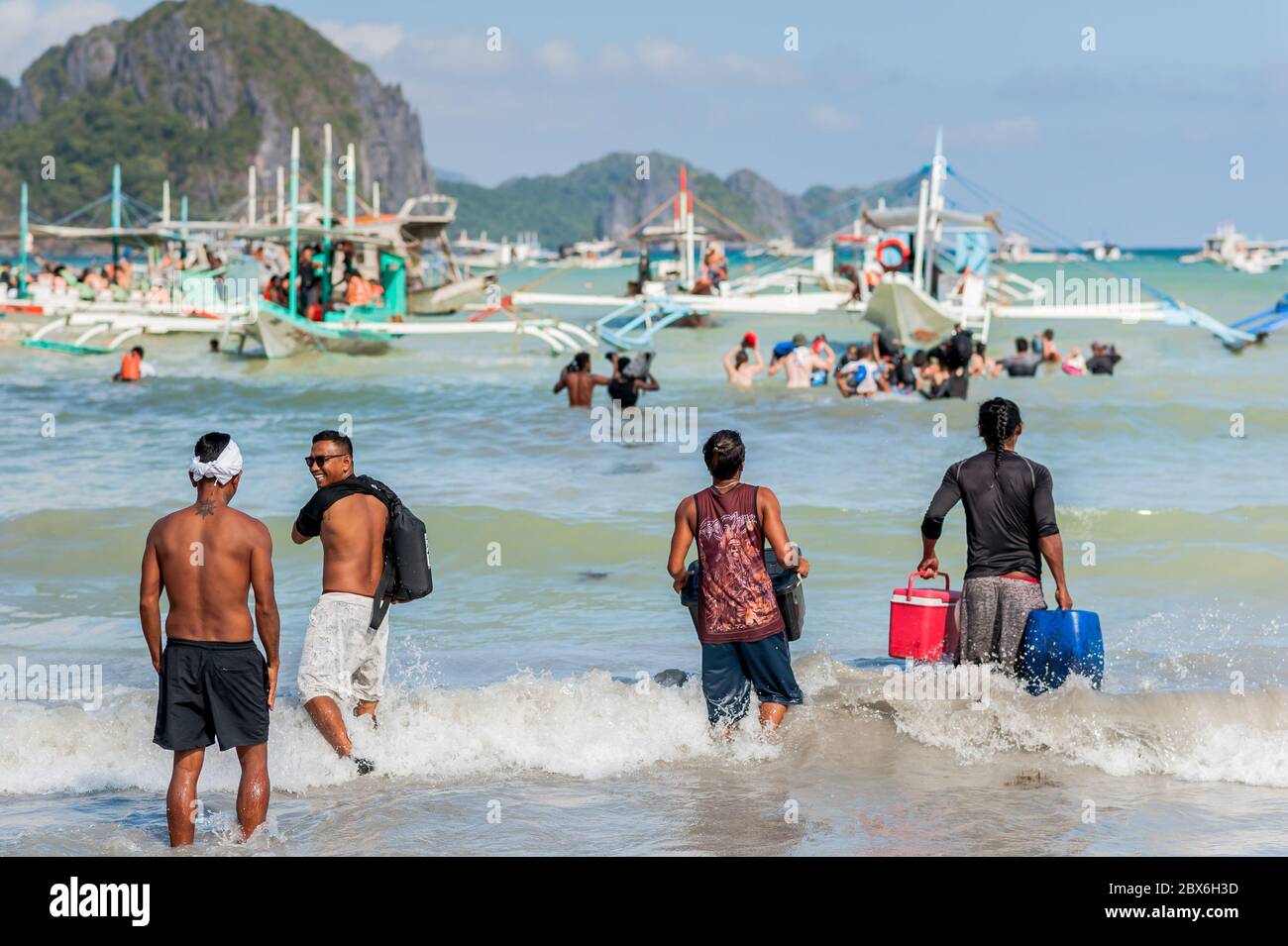 Les touristes et les mains de bateaux philippins locaux se sont emparés ou apportent des fournitures aux nombreux bateaux amarrés dans le surf attendant de visiter les îles et les plages. Banque D'Images