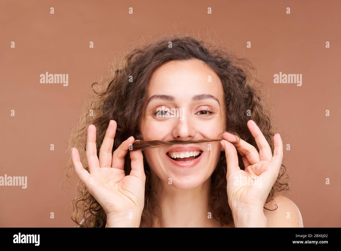 Jeune femme joyeuse avec un sourire crasseux tenant une bande de cheveux entre sa bouche et le nez tout en s'amusant et exprimant la joie Banque D'Images