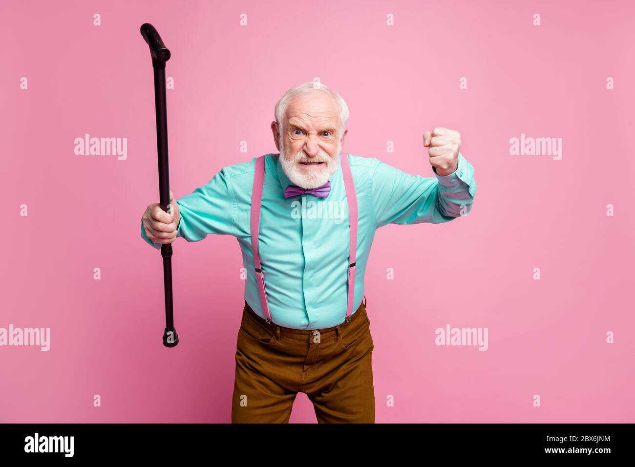 Photo d'un homme fou et âgé qui lève une canne à pied poing en colère grimace qui accuse les enfants voisins de comportement bruyant porter une chemise bretelles noeud cravate pantalon isolé Banque D'Images
