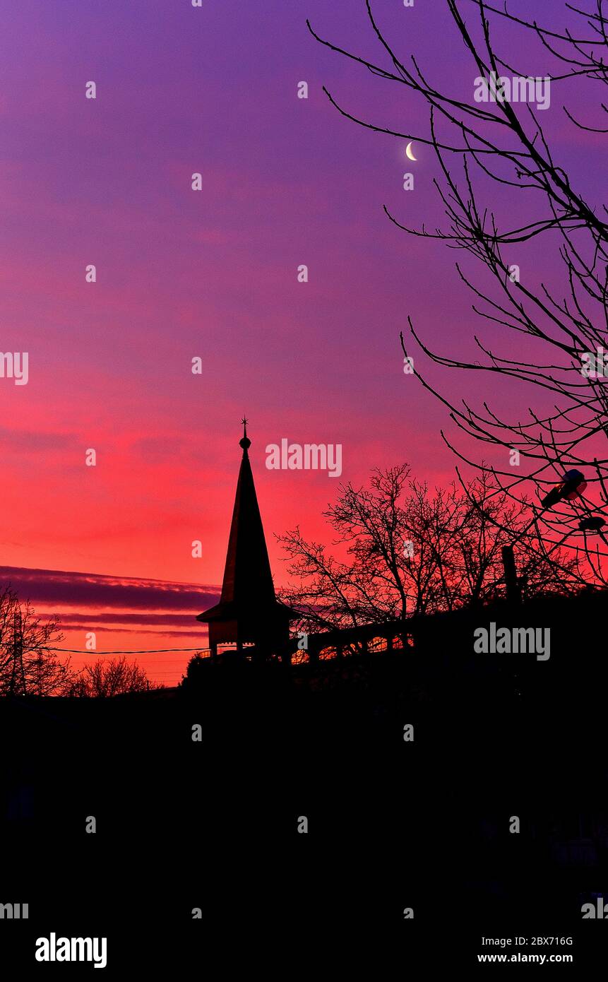 Ciel coloré au coucher du soleil avec des silhouettes d'une église et des arbres. Banque D'Images