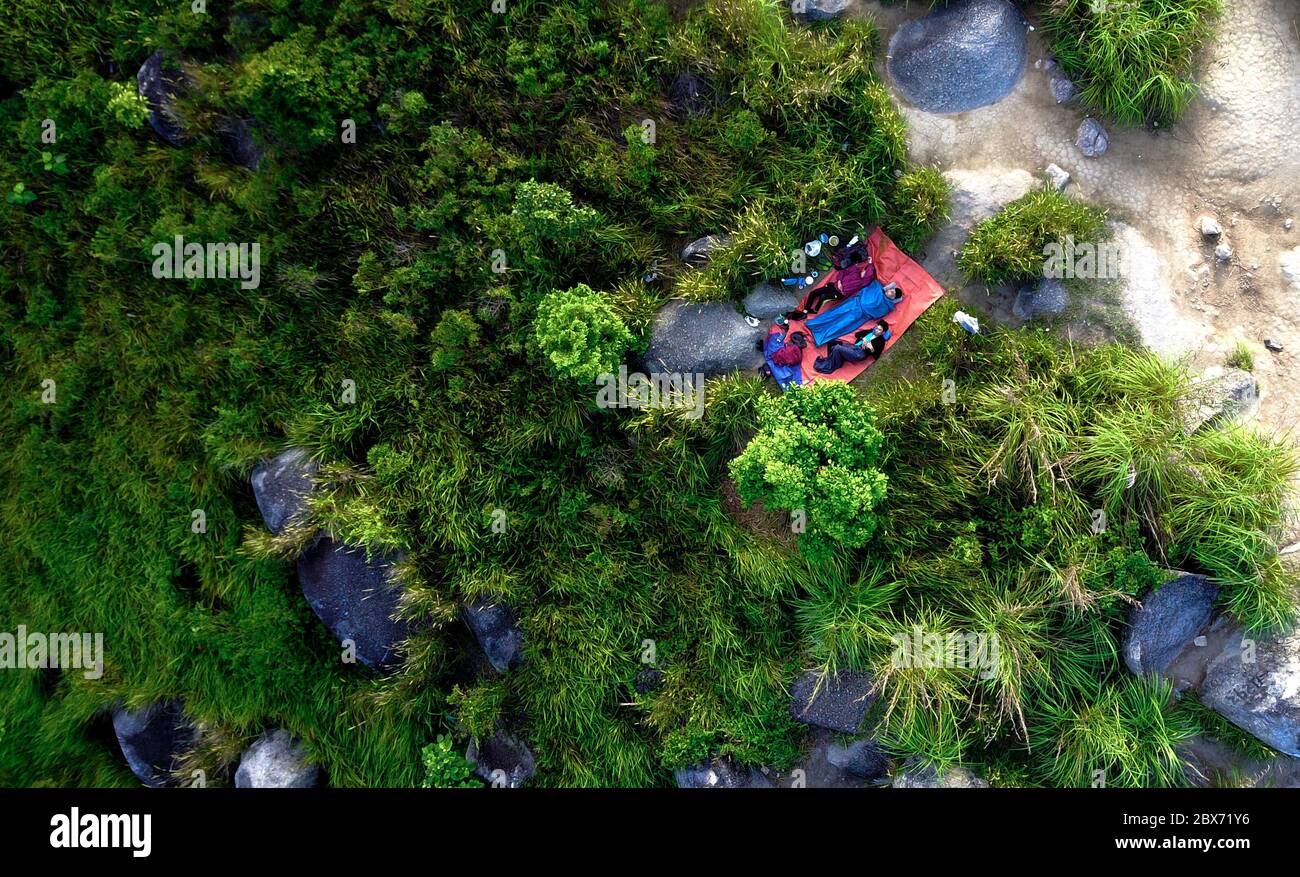 Vue aérienne de dessus en bas sur les touristes dormant dans un sac de couchage et un tapis, entre les plantes et les rochers Banque D'Images