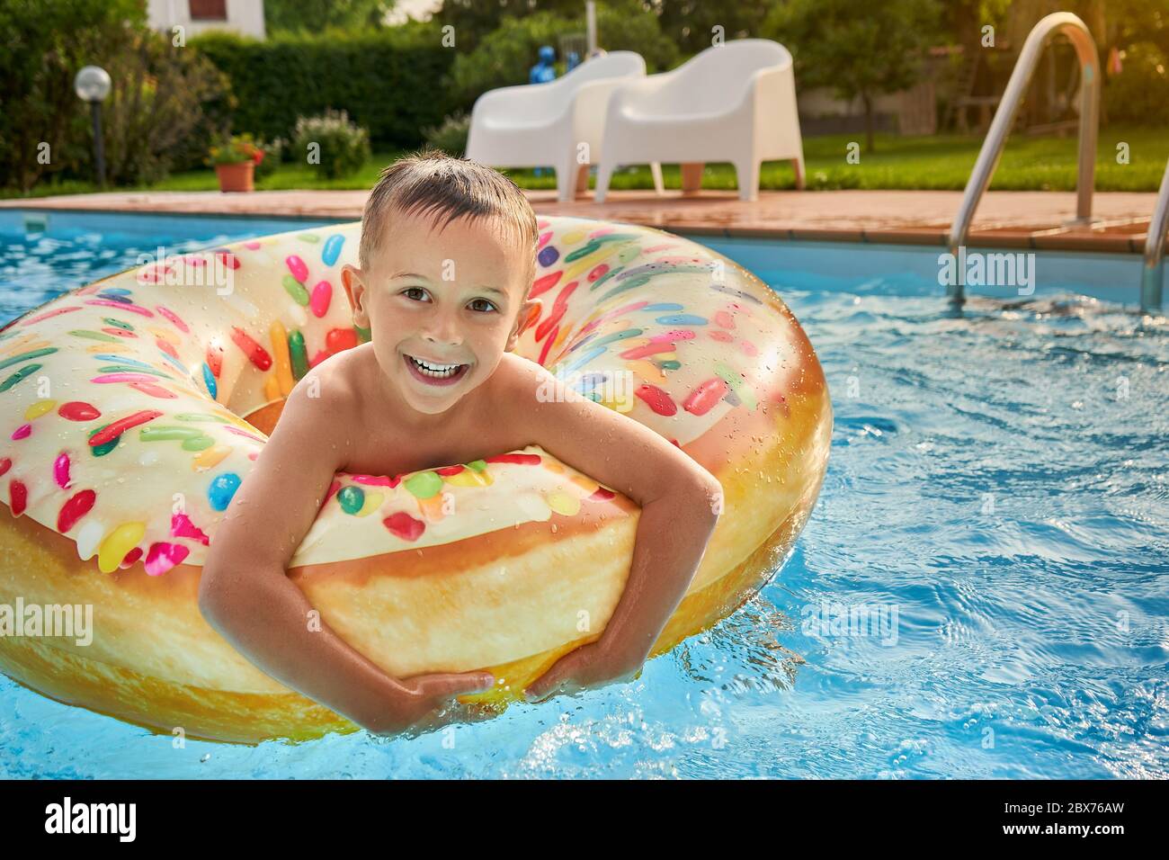 Garçon de 5 ans dans la piscine souriant sur l'anneau coloré gonflable, chaud jour d'été en vacances Banque D'Images