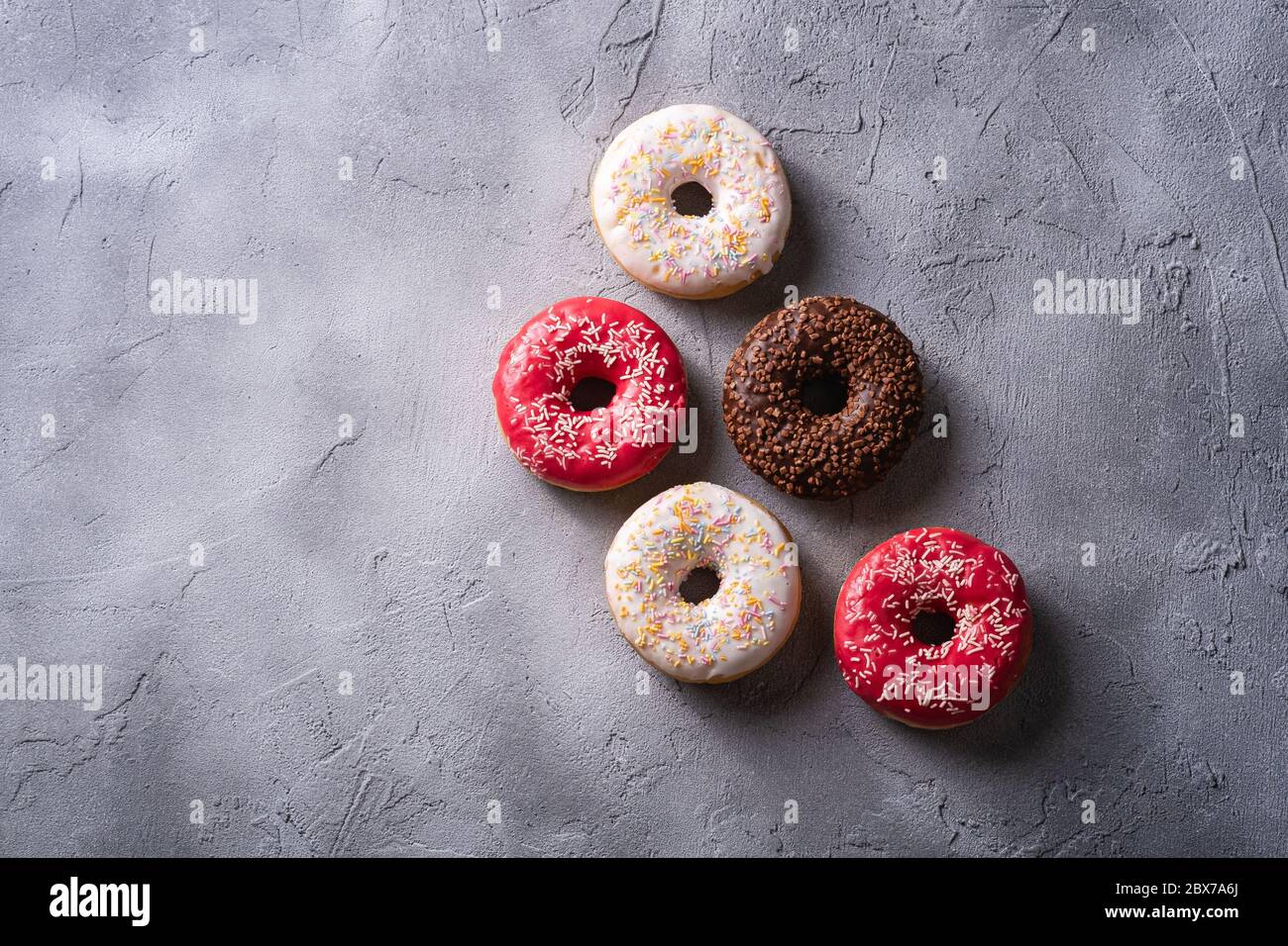 Beignets au chocolat, roses et vanille avec saupoudrés, desserts glacés sur fond de béton texturé, espace de photocopie avec vue sur le dessus Banque D'Images