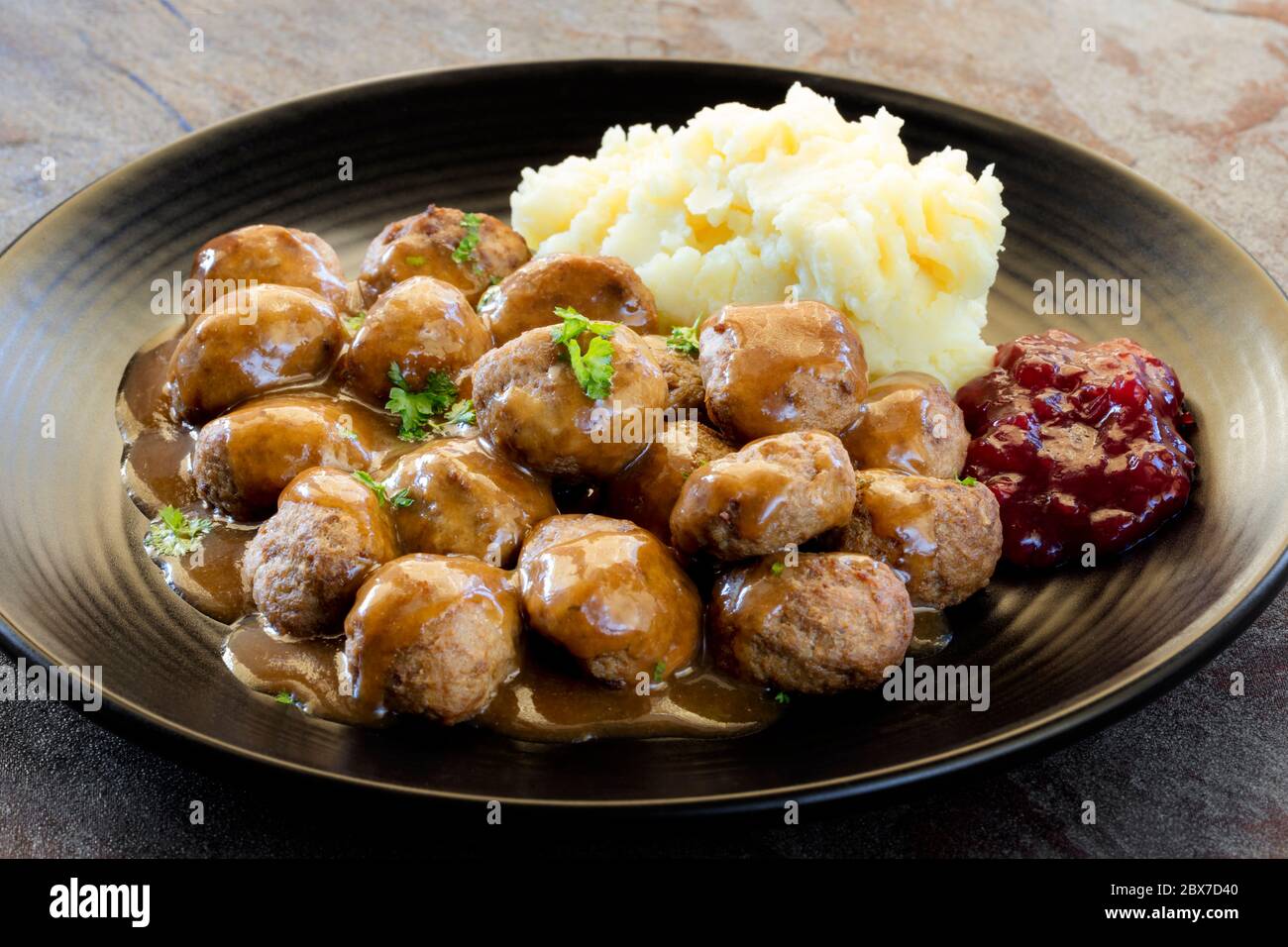 Boulettes de viande suédoises avec purée de pommes de terre, sauce et baies de lingonberry sur une assiette noire. Vue latérale, sur ardoise. Banque D'Images