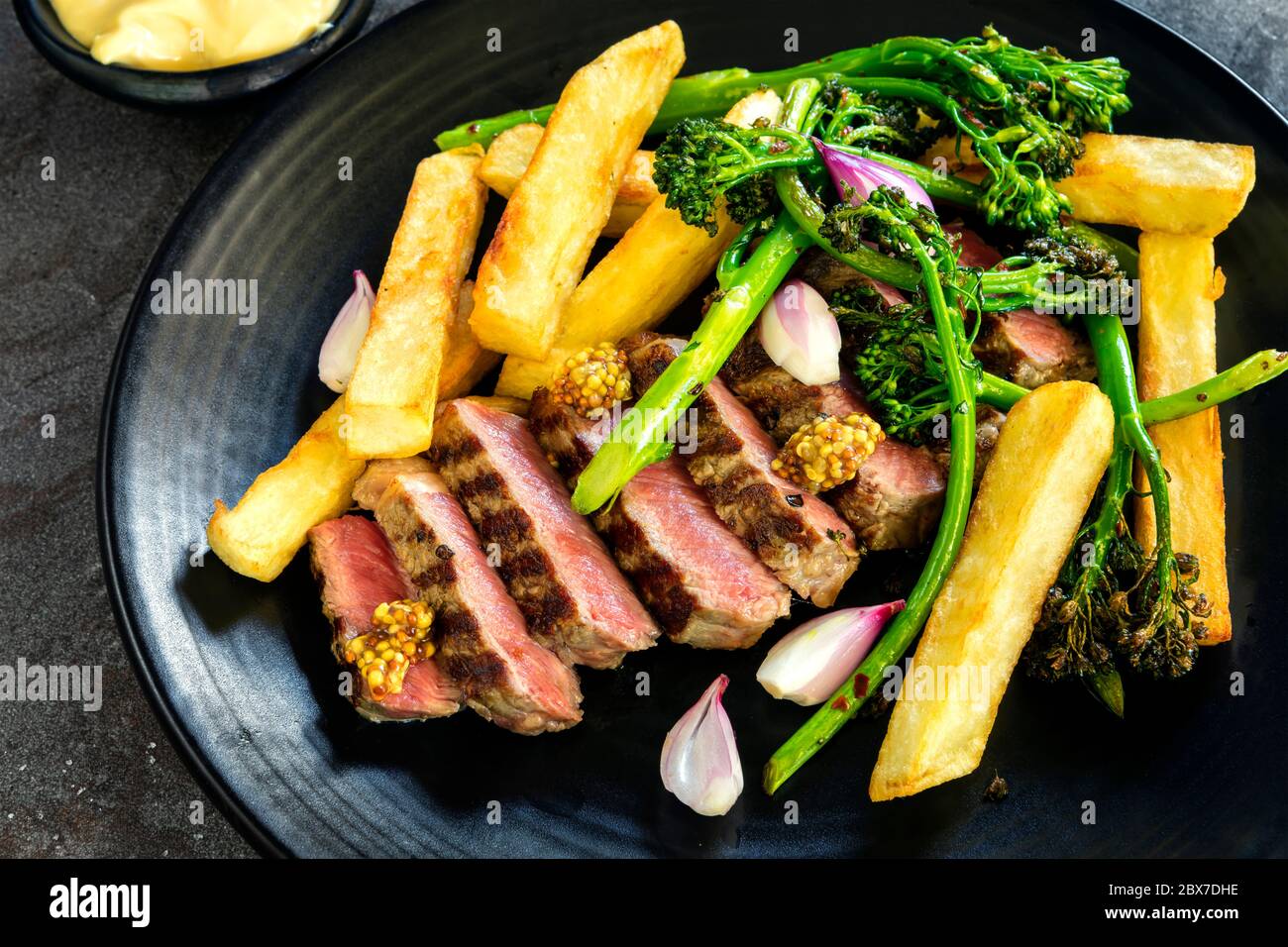 Steak et frites au broccolini, moutarde à la baleine, échalotes marinées et sauce béarnaise. Portreuse en tranches. Banque D'Images