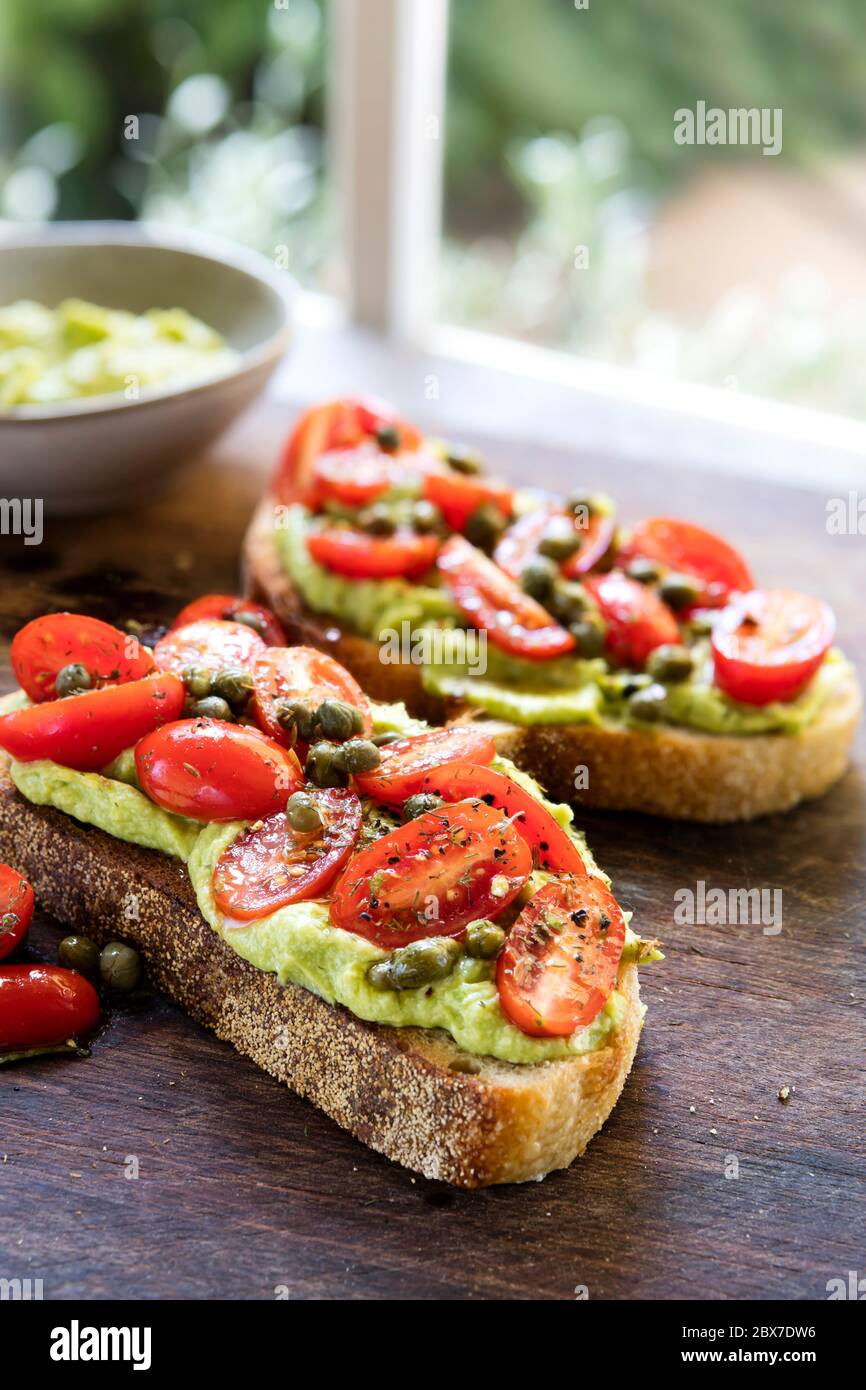 Toast à l'avocat avec tomates cerises et salsa au câpres. Pain au levain. Sur la vieille planche, avec vue sur le jardin derrière. Banque D'Images