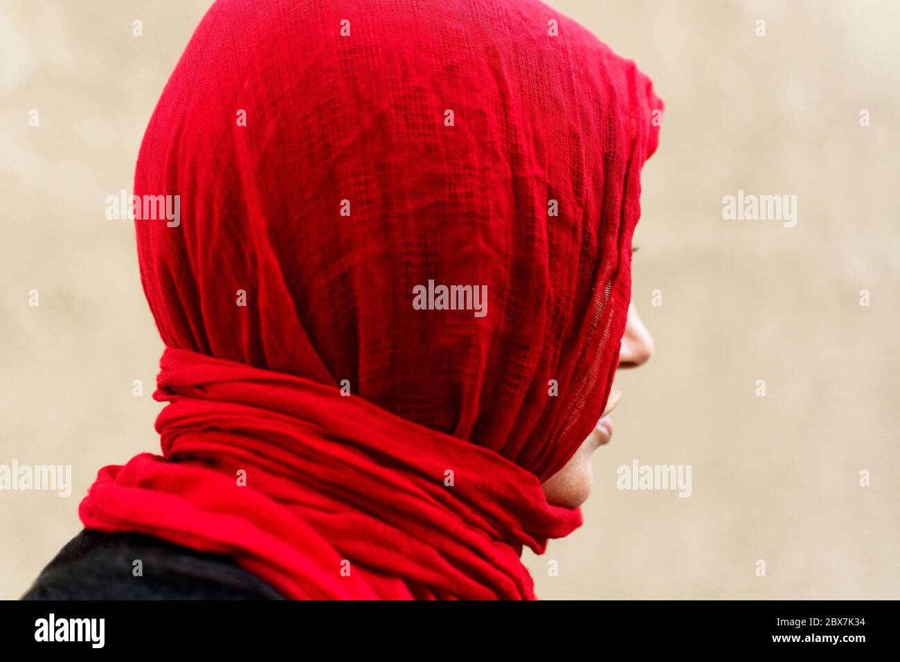 Profil de la jeune femme belle portant un hijab rouge et un chandail noir sur un fond neutre. Éclairage naturel diffusé. Banque D'Images