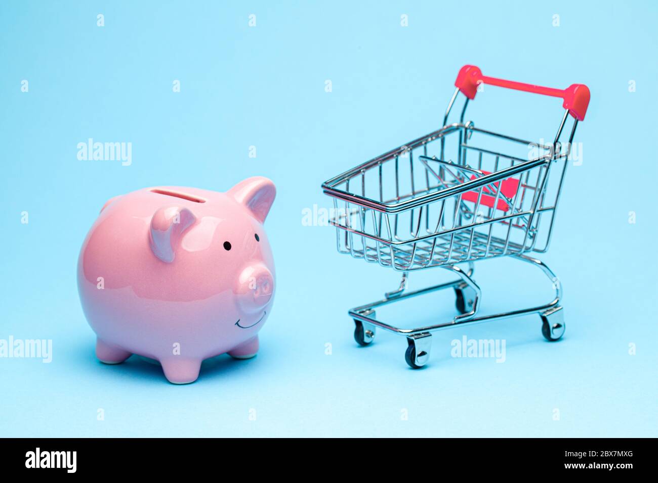 Banque de porc rose et chariot sur fond bleu. Le concept d'économie d'argent sur les achats dans le magasin Banque D'Images
