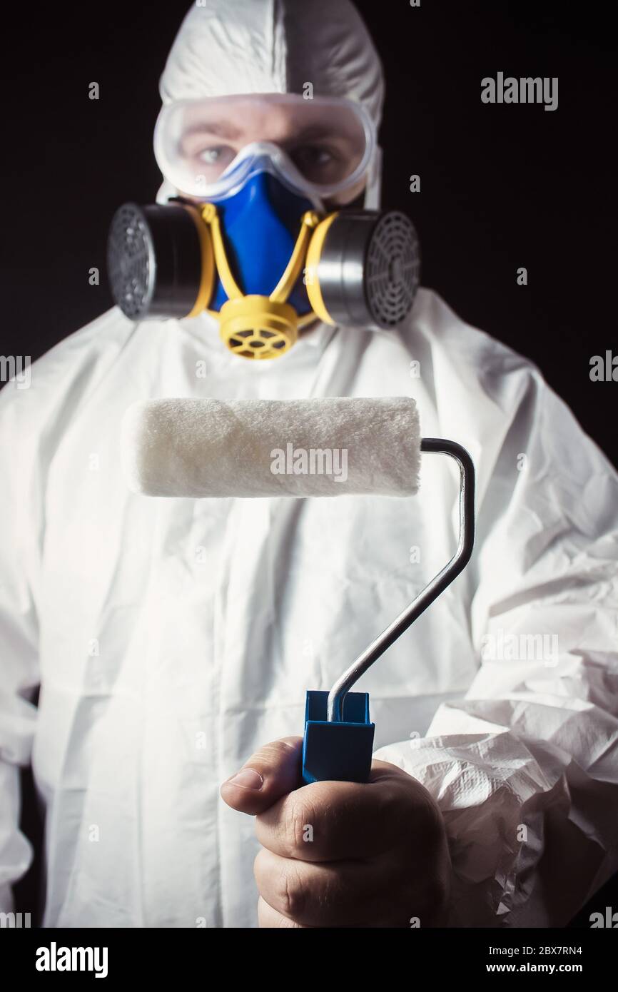 Travailleur en costume de protection et respirateur tenant un rouleau de peinture dans sa main vue rapprochée sur fond noir. Banque D'Images