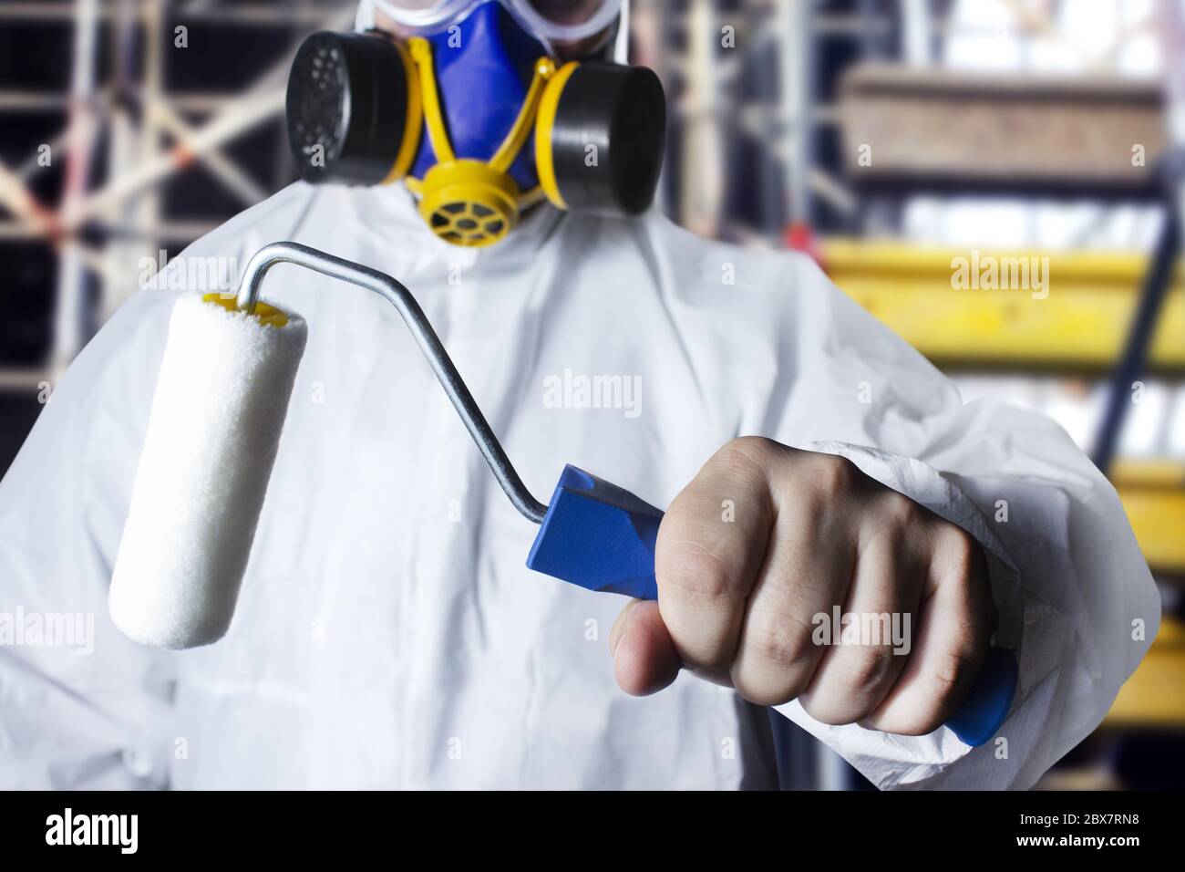 Travailleur en costume de protection et respirateur tenant un rouleau de peinture dans sa main, vue rapprochée sur le fond de la zone de construction. Banque D'Images