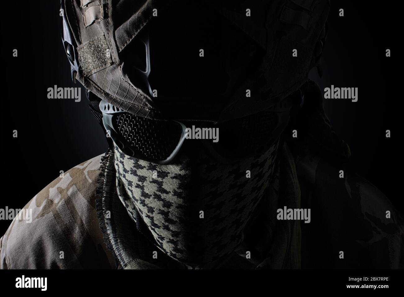 Tête de soldat militaire avec casque de camouflage, lunettes de protection et foulard militaire vue rapprochée sur fond noir. Banque D'Images