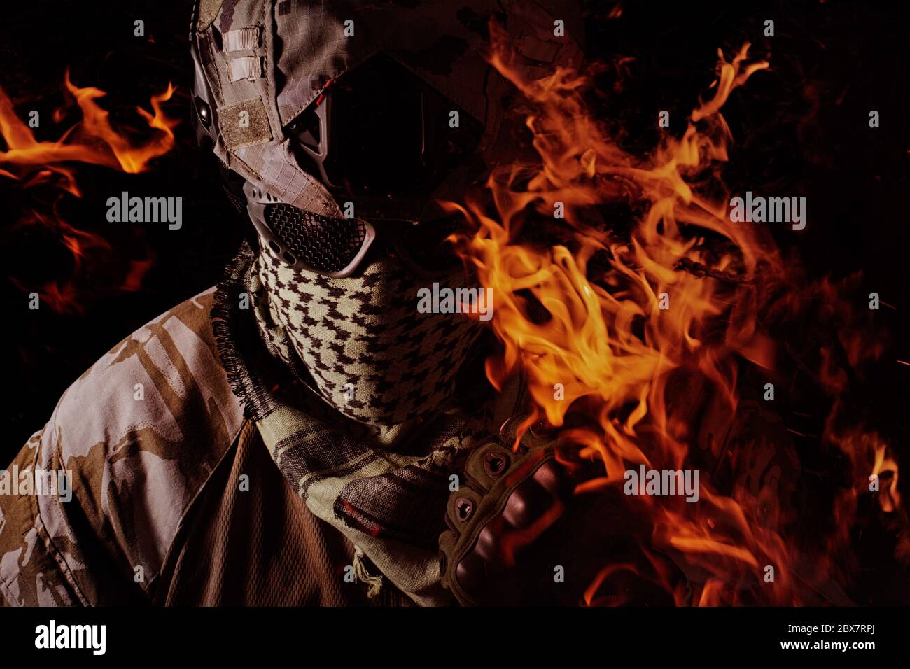 Portrait de soldat militaire avec main brûlante, casque de camouflage, lunettes de protection et foulard militaire vue rapprochée sur fond noir. Banque D'Images