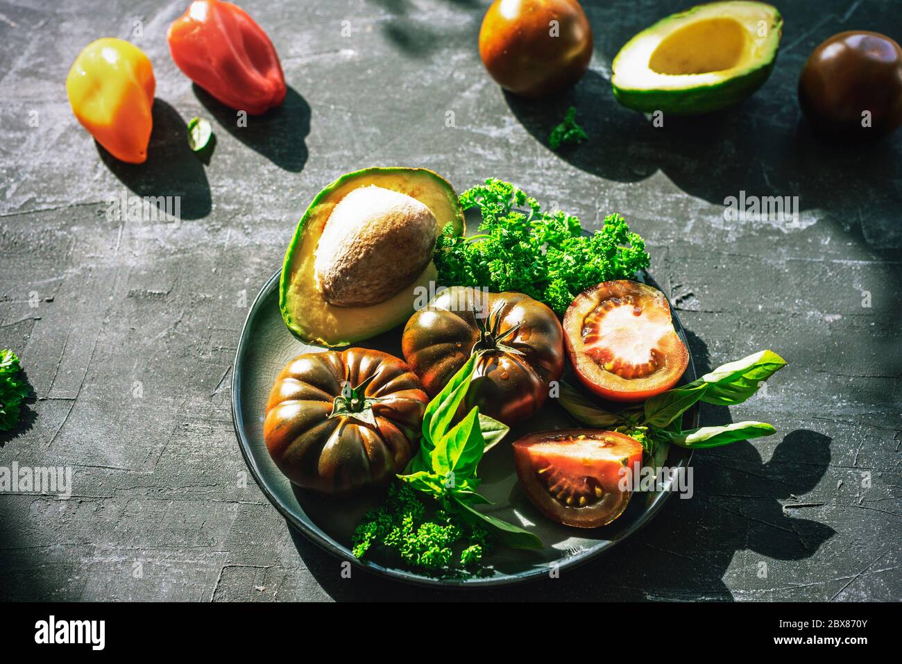 Avocat, tomates et autres légumes crus sur une assiette noire, vue du dessus. Concept d'alimentation saine Banque D'Images