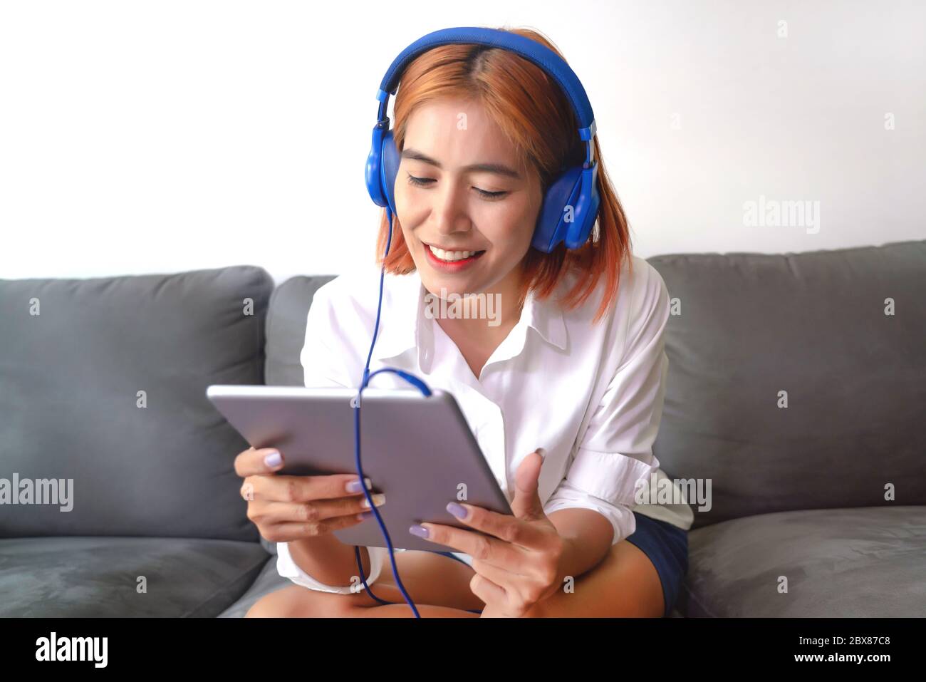 La jeune femme asiatique est heureuse de travailler à la maison. Elle utilise une tablette pour discuter par vidéo avec ses collègues d'une entreprise. Banque D'Images