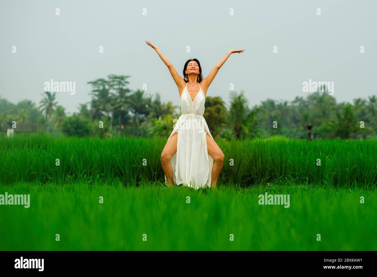 Corps et esprit connexion avec la nature - heureuse et belle asiatique japonaise femme faisant yoga et méditation exercice à l'extérieur à l'idyllique vert fiel de riz Banque D'Images