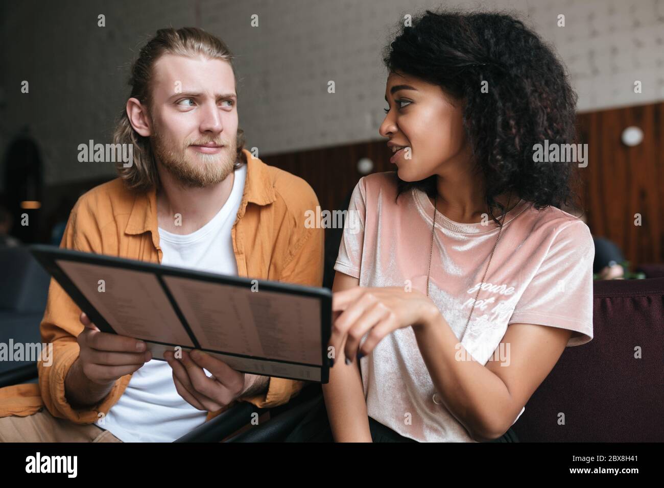 Portrait d'un jeune homme et d'une fille assis au restaurant avec menu  entre les mains. Jolie fille américaine africaine aux cheveux fclés foncés  et garçon aux cheveux blonds Photo Stock - Alamy